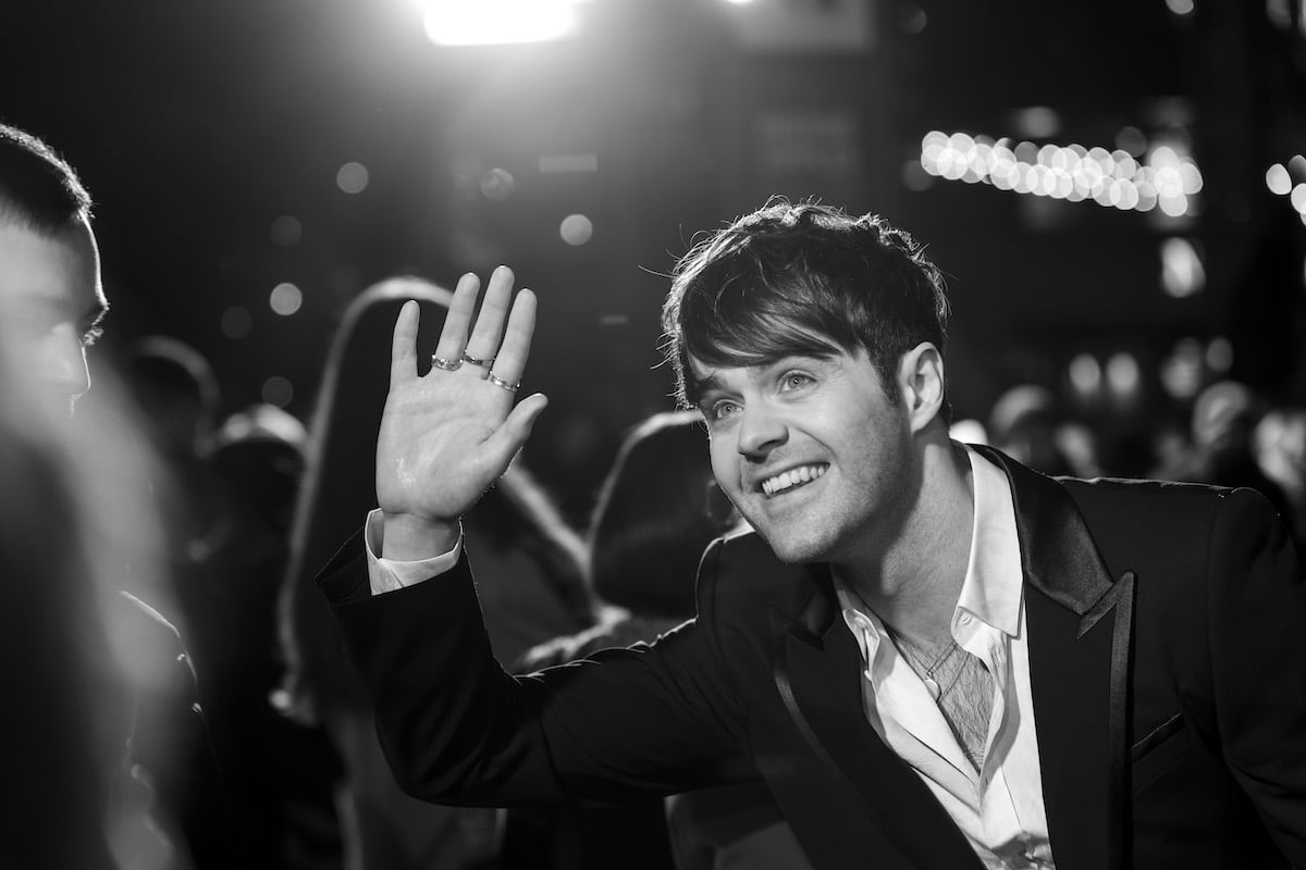 Actor Joey Batey waves to fans in a black and white photo taken at "The Witcher: Blood Origin" premiere.