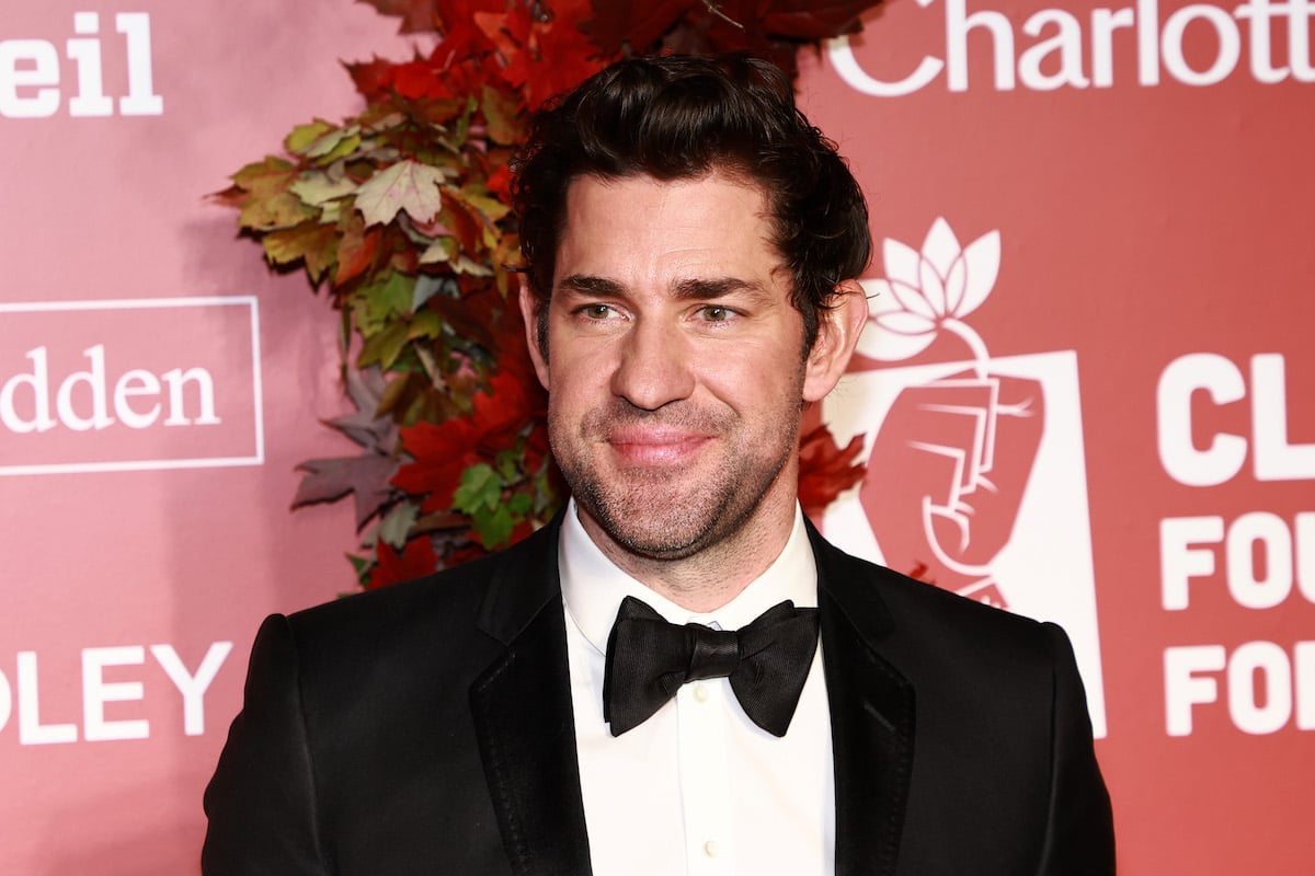 John Krasinski poses for photos at an event against a pink backdrop.