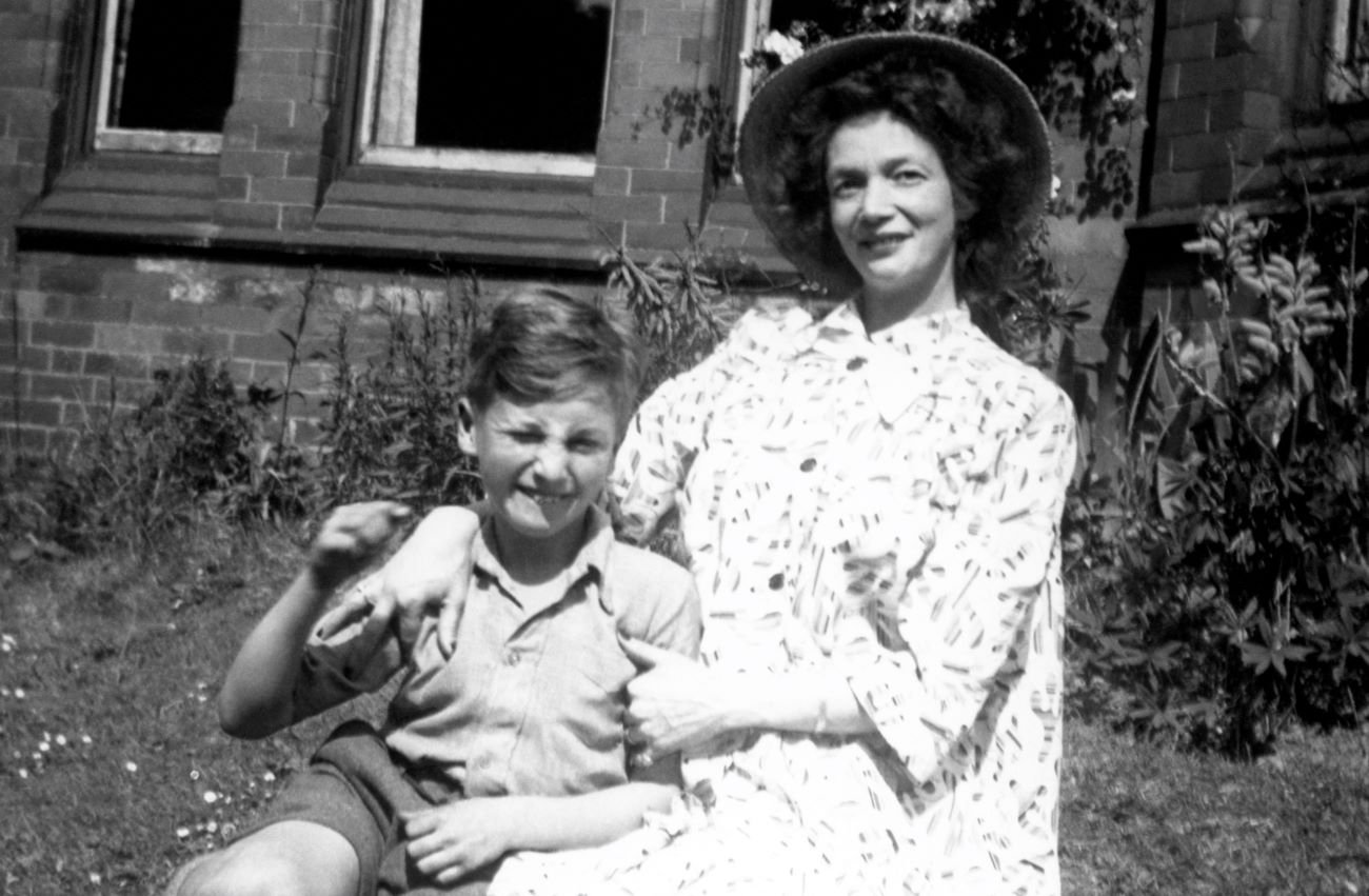 A black and white picture of a young John Lennon and his mother, Julia, sitting outside together.