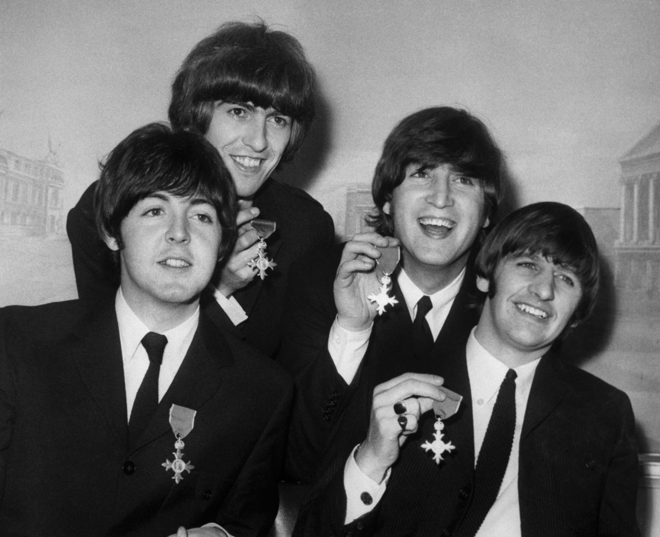 A black and white picture of Paul McCartney, George Harrison, John Lennon, and Ringo Starr holding medals they received from Queen Elizabeth.