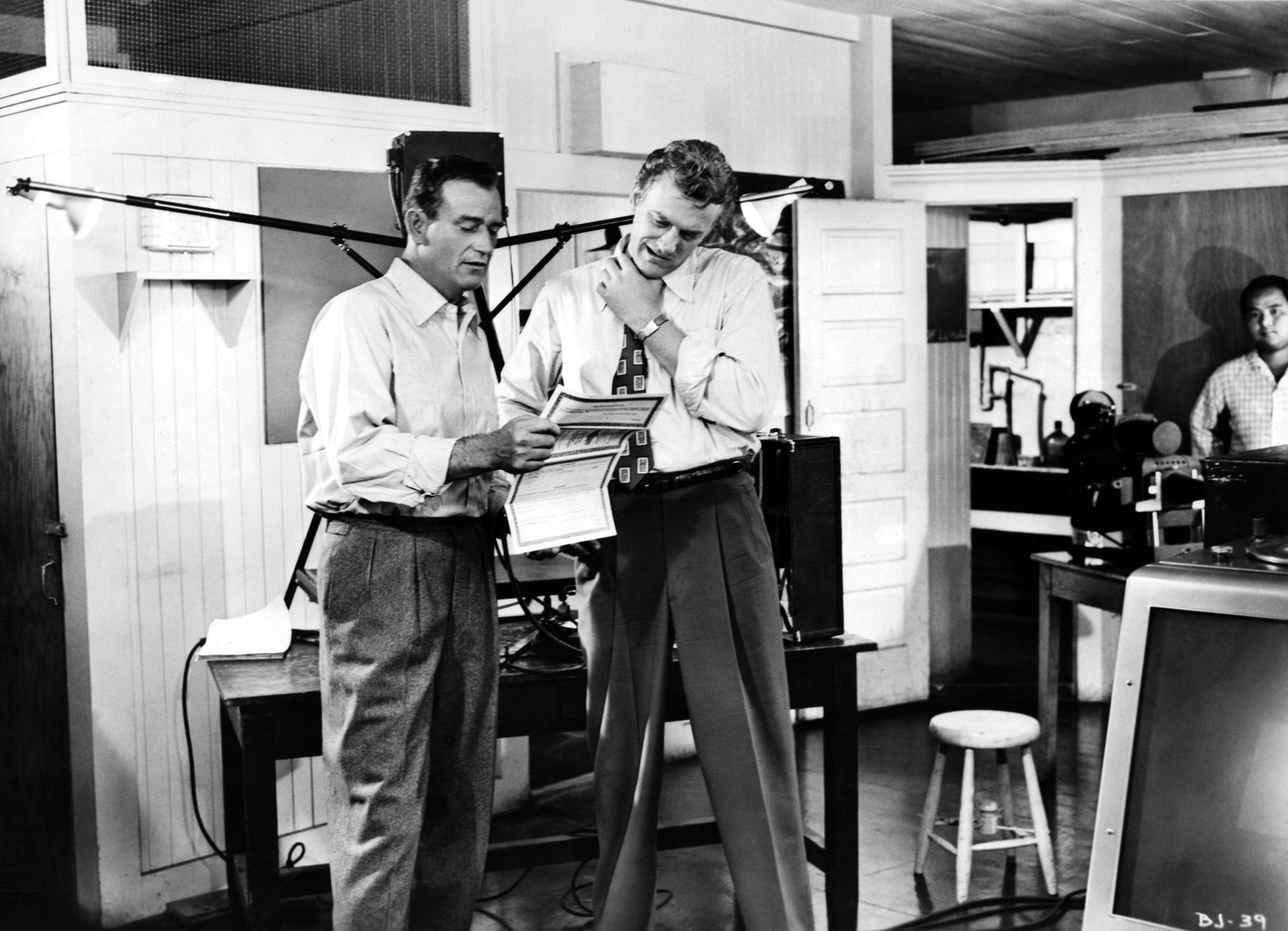 John Wayne and 'Gunsmoke' actor James Arness in a black-and-white photograph on the set of 'Big Jim McLain' wearing dress shirts and dress pants