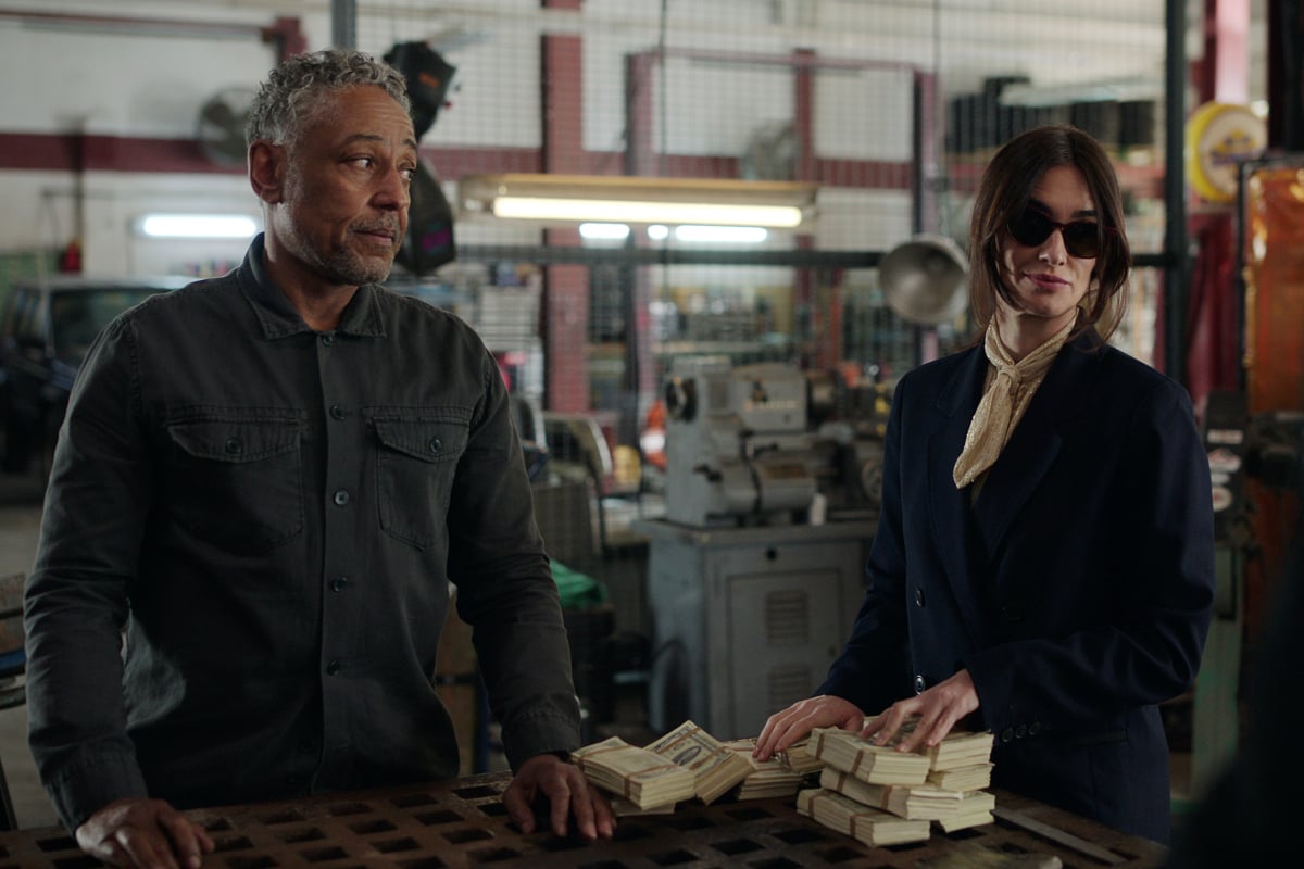 In the Netflix series Kaleidoscope, Leo and Ava stand next to bundles of cash.