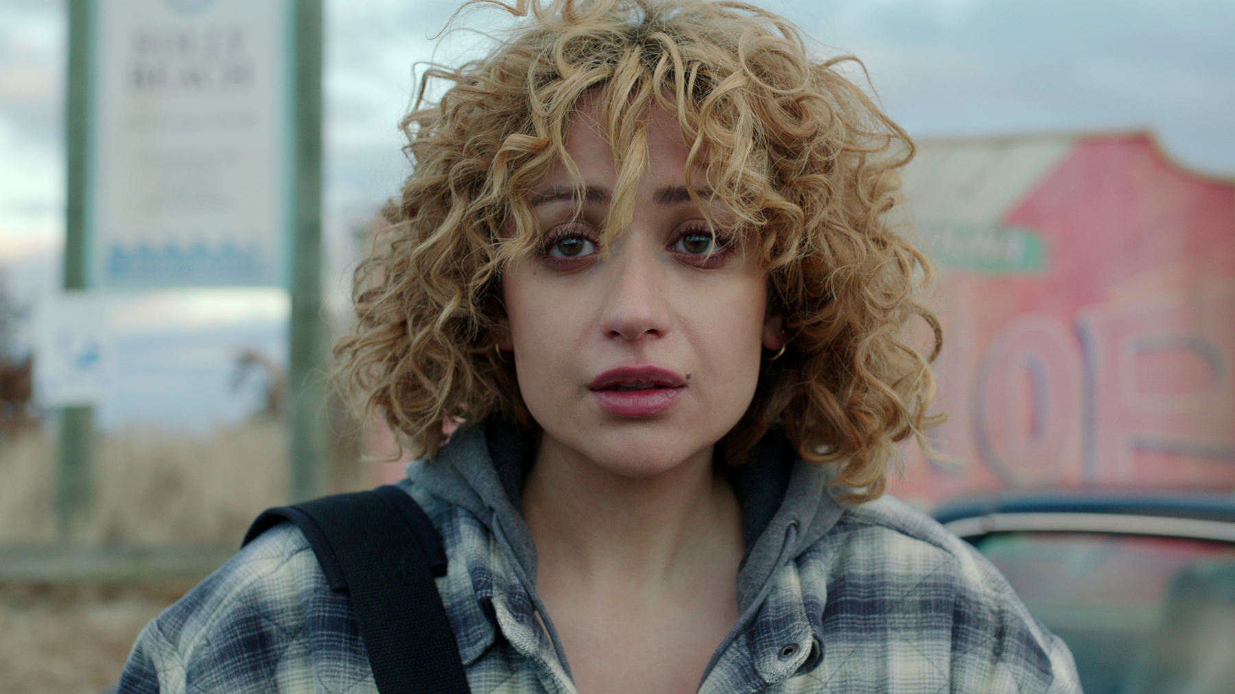 Actor Rosaline Elbay, who plays Judy Goodwin in 'Kaleidoscope' on Netflix. Her hair is blonde and curly, and she's wearing a blue and white flannel shirt.