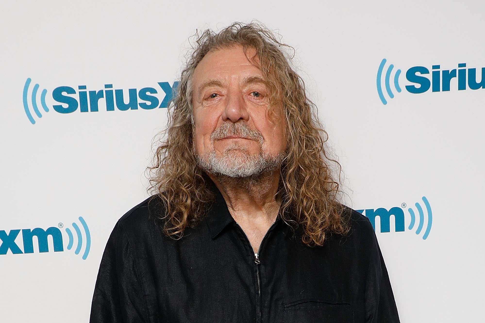 Robert Plant wears black and stands in front of a white background.