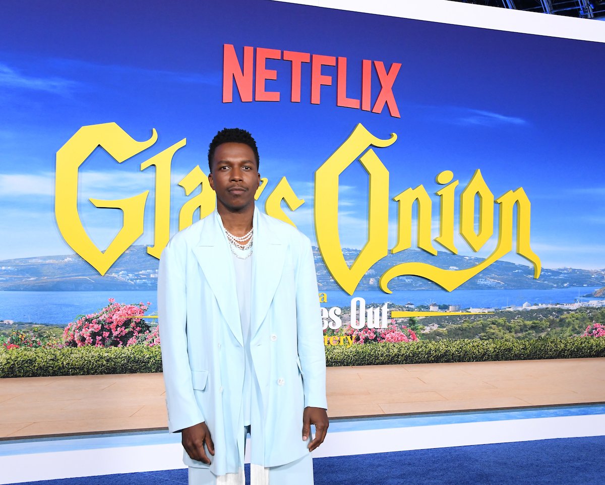 Leslie Odom Jr. poses for cameras in front of the logo of "Glass Onion" at a premiere event.