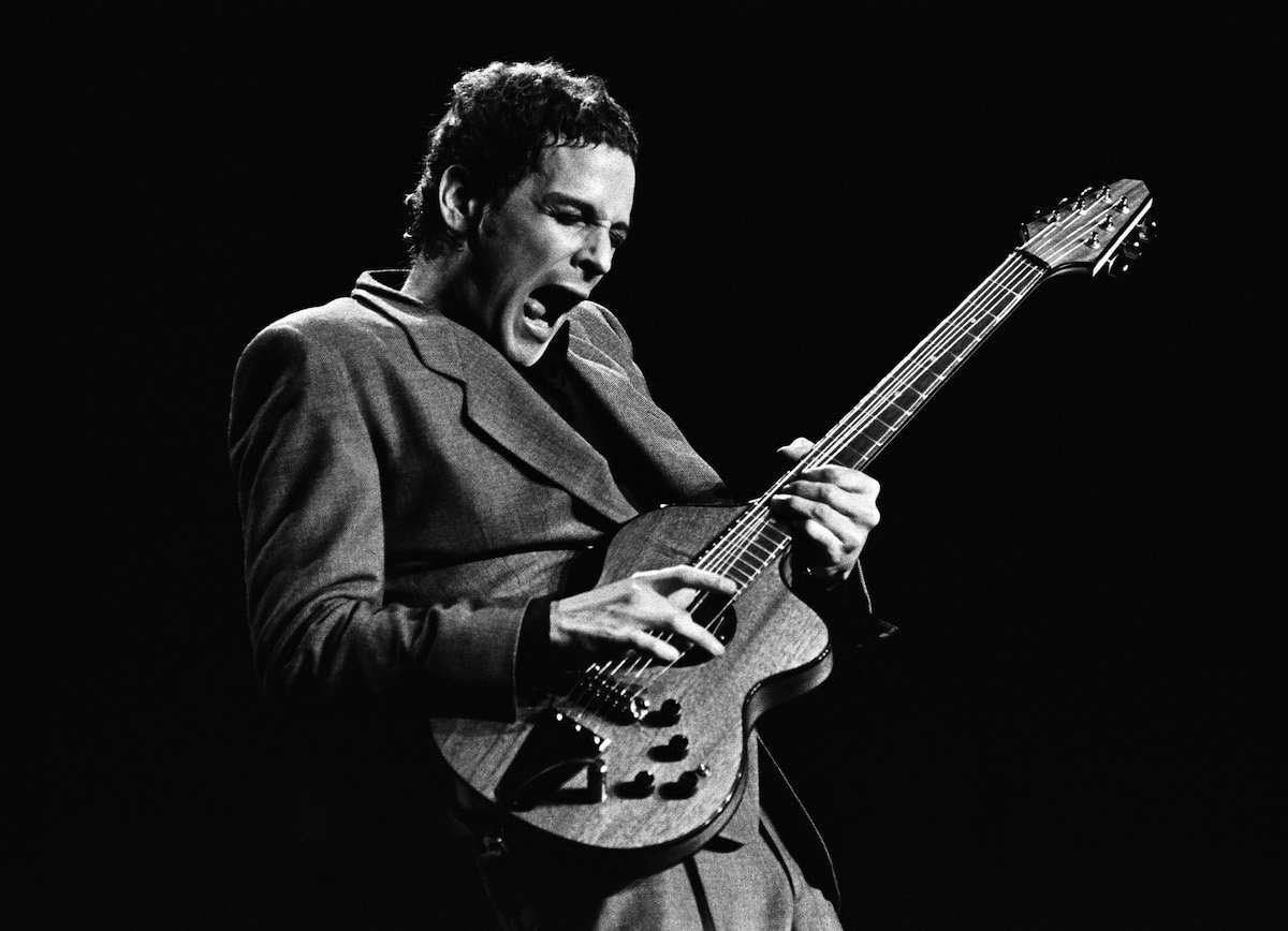 A black and white photo of Fleetwood Mac guitarist Lindsey Buckingham performing on stage.