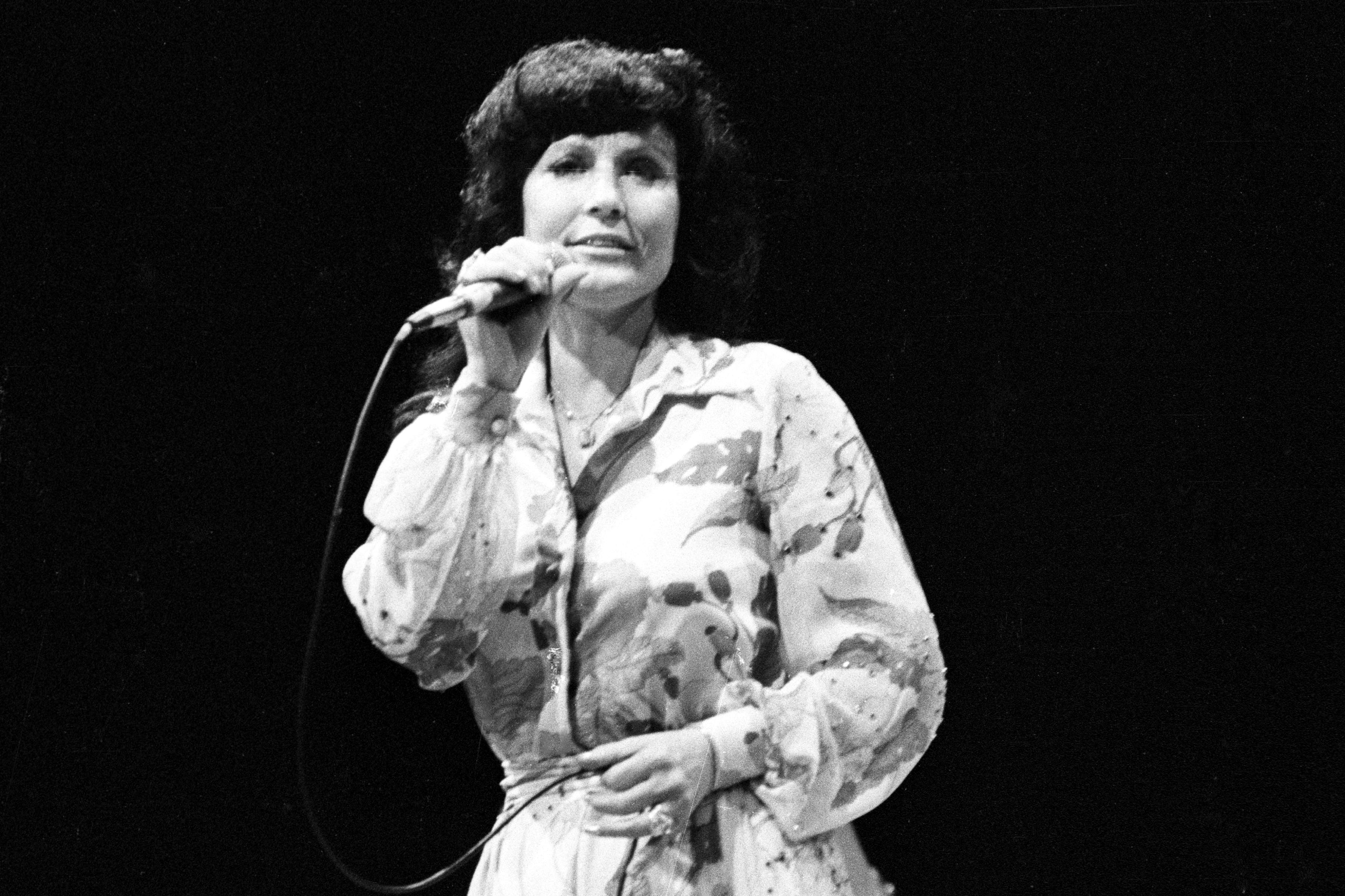 A black-and-white photo of Loretta Lynn holding a microphone