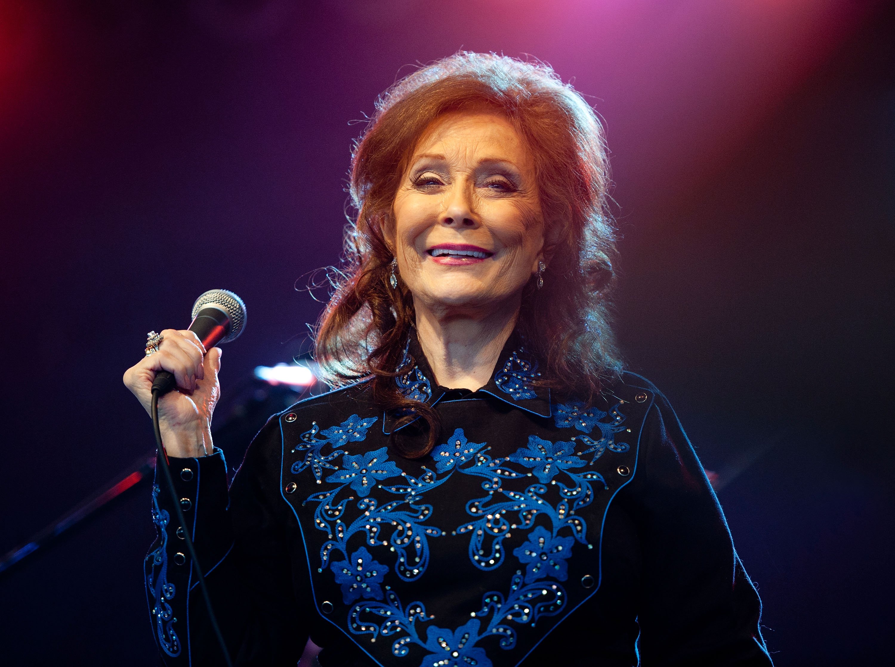 Loretta Lynn stands onstage holding a microphone
