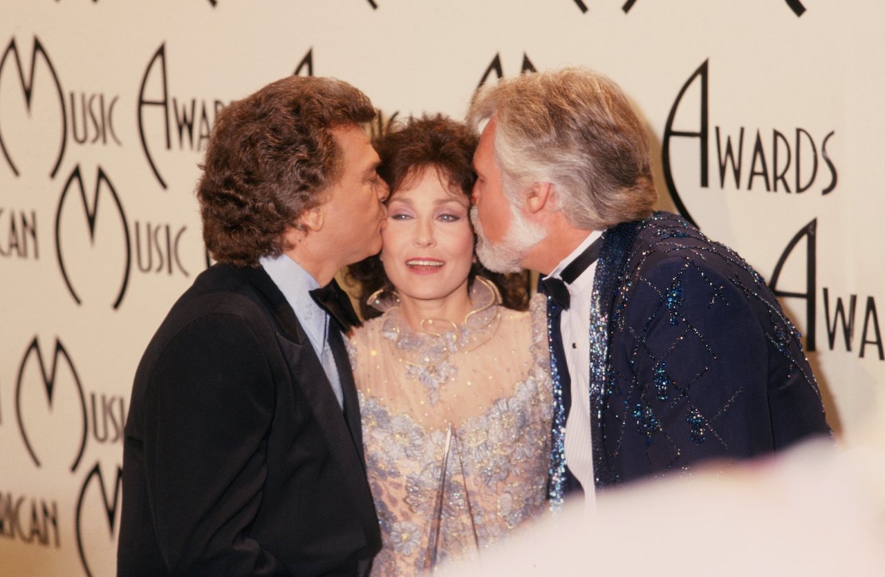 Loretta Lynn poses for a portrait as Conway Twitty (L) and Kenny Rogers (R) each kiss a cheek at the American Music Awards which were held at the Santa Monica Civic Auditorium on January 16, 1978, in Santa Monica, California.
