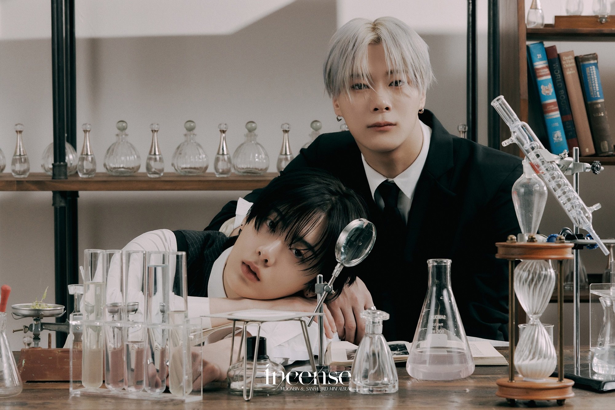 The ASTRO sub-unit MOONBIN&SANHA pose behind beakers sitting on a desk