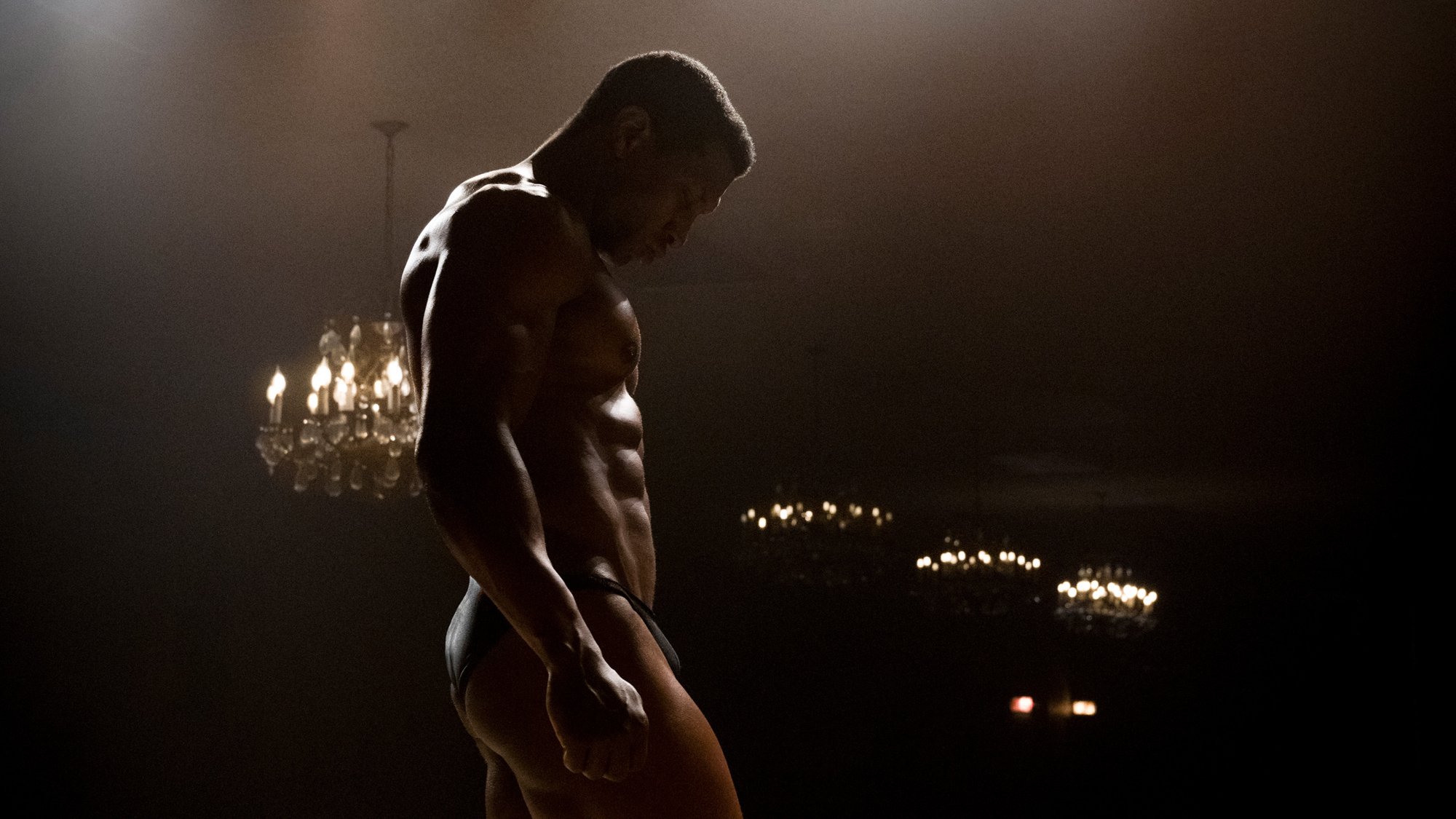 'Magazine Dreams' Jonathan Majors as Killian Maddox wearing a speedo, standing in a dark room with chandeliers