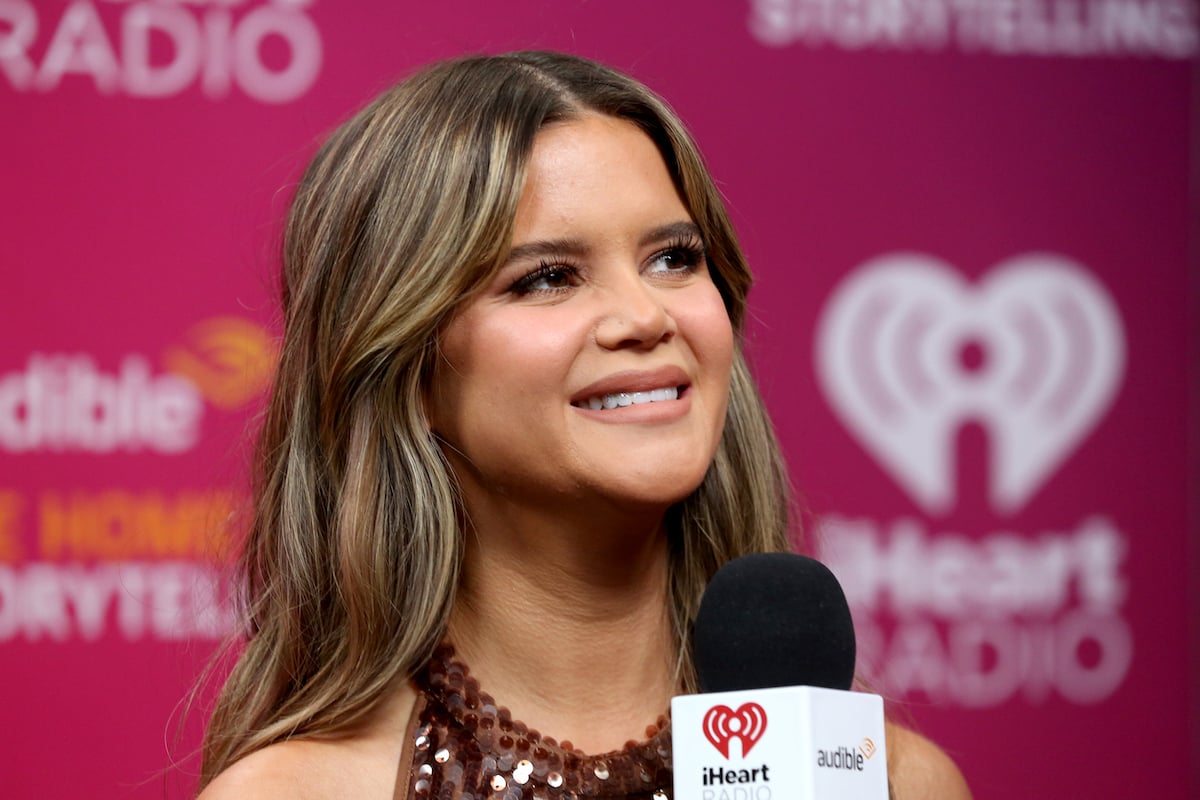 Maren Morris speaks into a microphone in front of an iHeartRadio backdrop