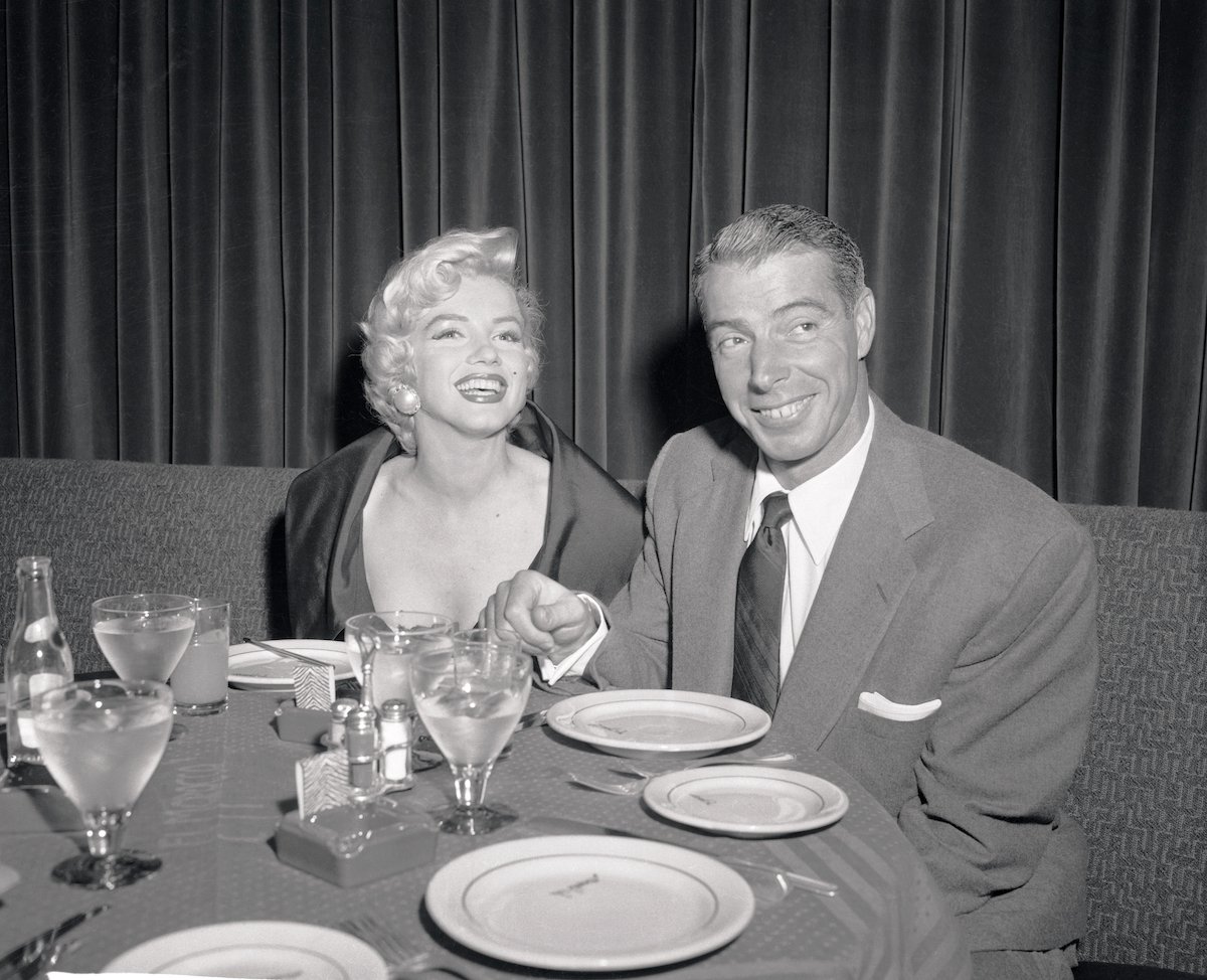 Marilyn Monroe and Joe DiMaggio smiling, sitting at a dinner table, in black and white