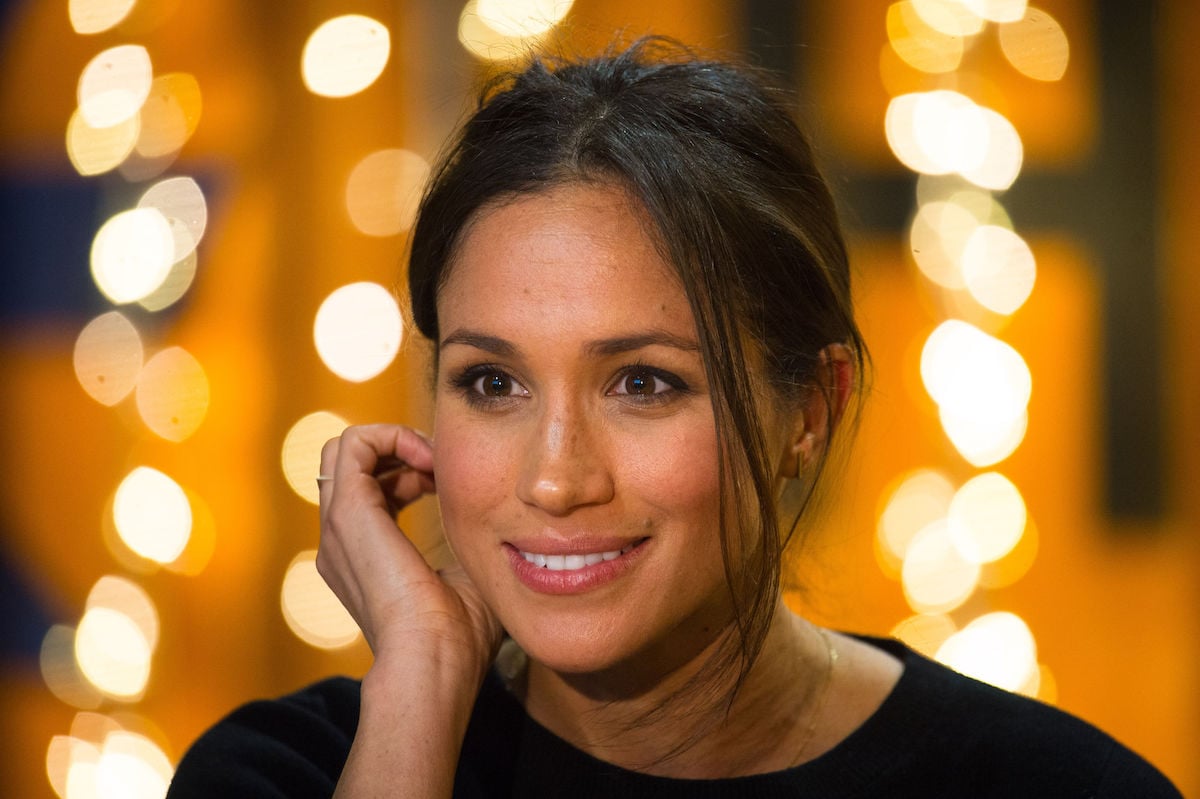 Meghan Markle, who served marijuana at her first wedding before meeting Prince Harry, smiles with one hand held up to her face.