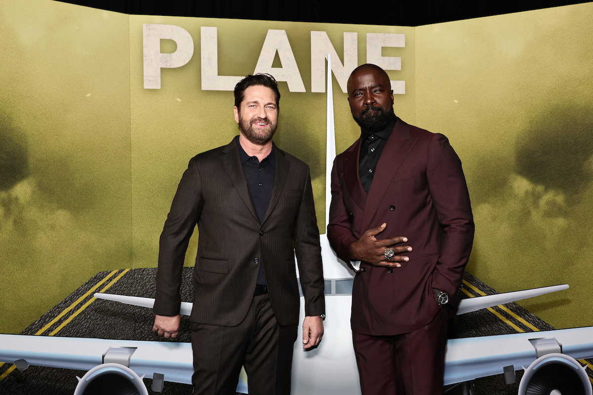 Actors Mike Colter and Gerard Butler pose in front of a cardboard cutout featuring key art from the film "Plane."