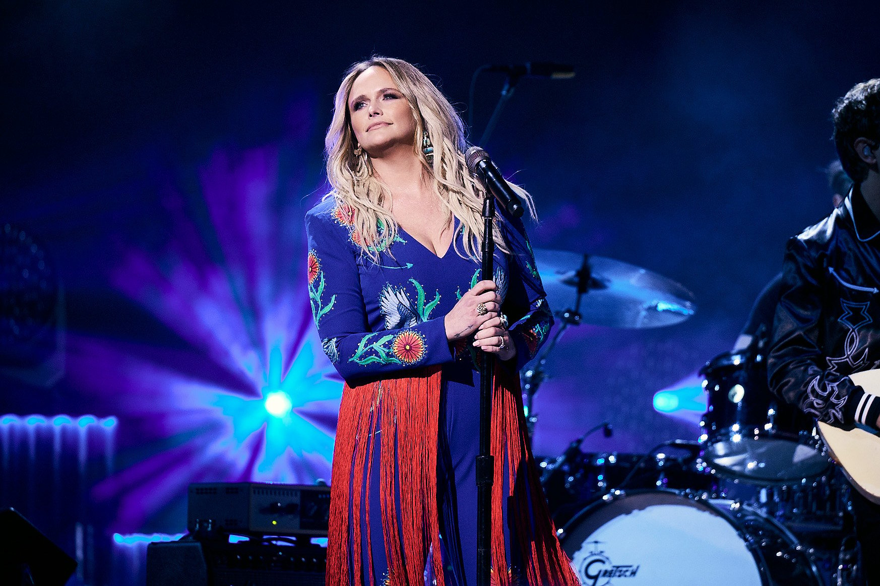 Miranda Lambert holds a microphone stand while wearing a blue-and-red outfit