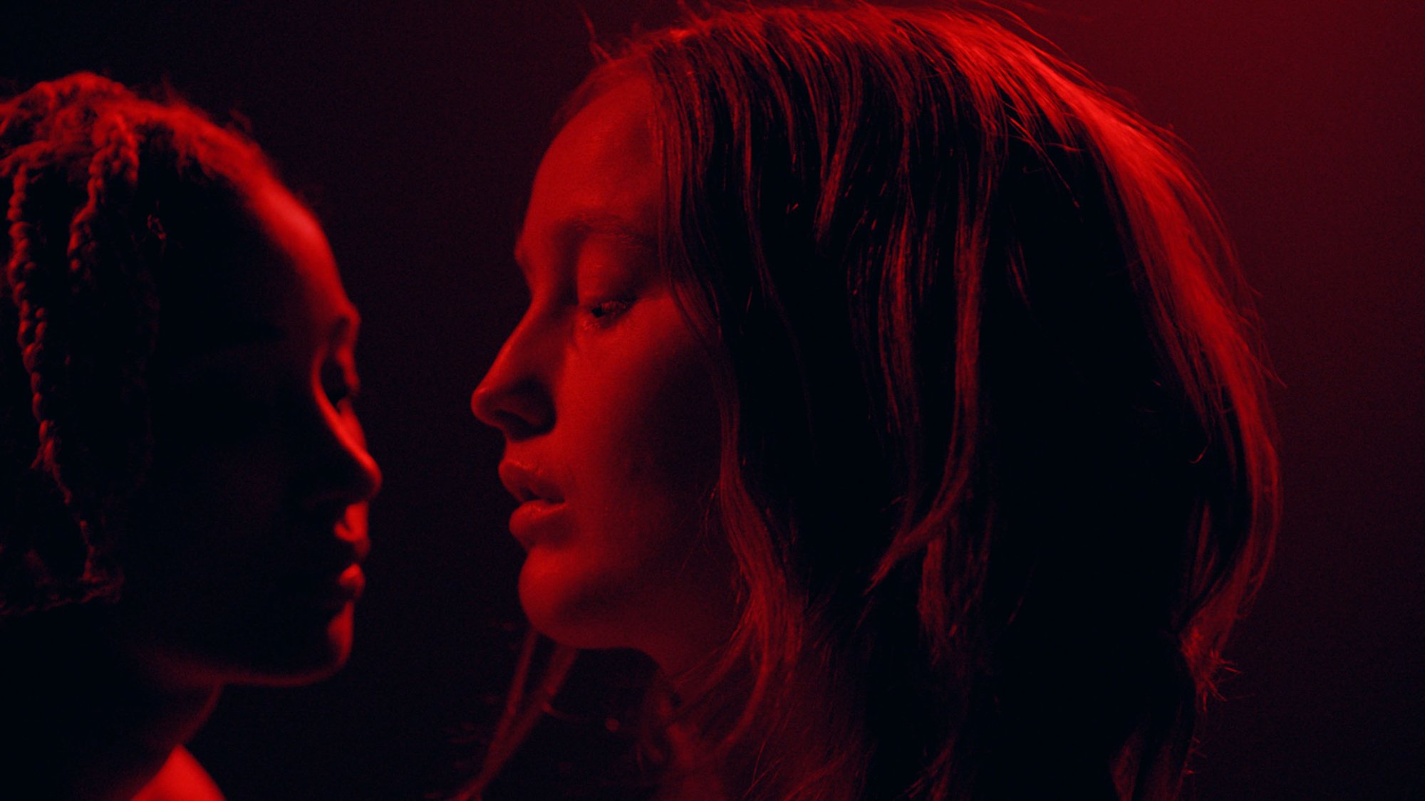 'My Animal' Amandla Stenberg as Jonny and Bobbi Salvör Menuez as Heather with their faces together in red lighting