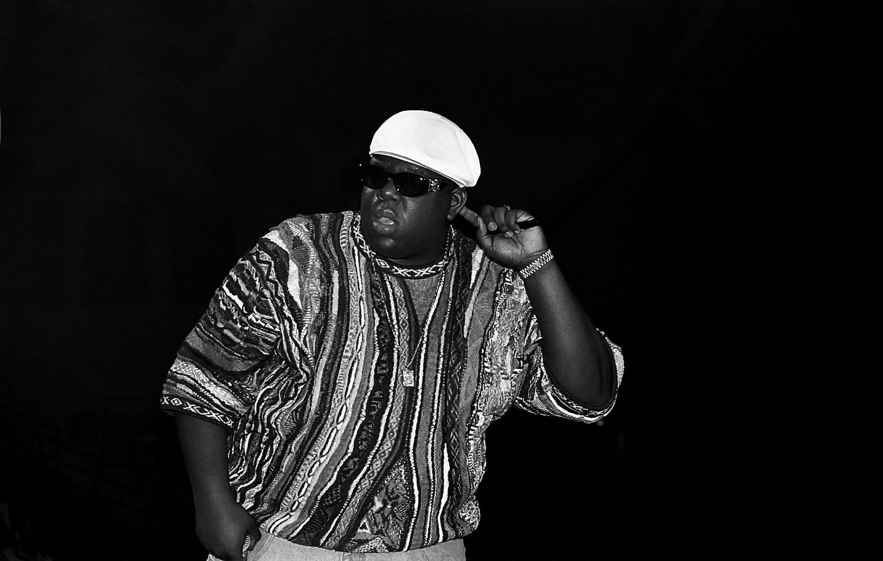 The Notorious B.I.G., rapper behind hit songs like 'Juicy' and 'Big Poppa,' on stage wearing a striped shirt and white hat