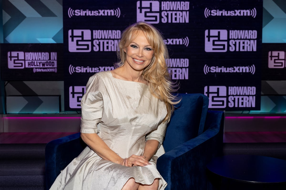 Pamela Anderson poses for a photo in front of a backdrop featuring the logo for The Howard Stern Show