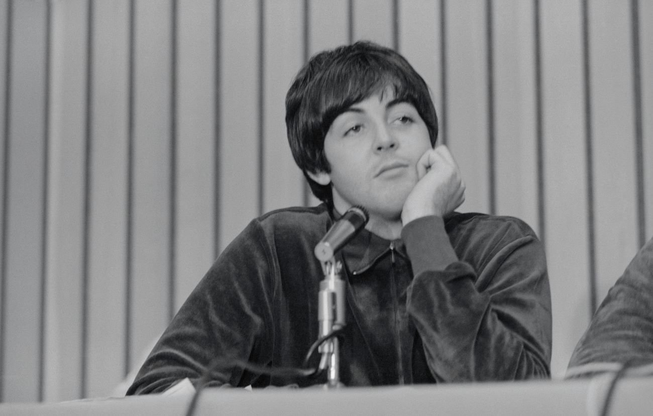 A black and white picture of Paul McCartney sitting in front of a microphone with his chin resting on his hand.