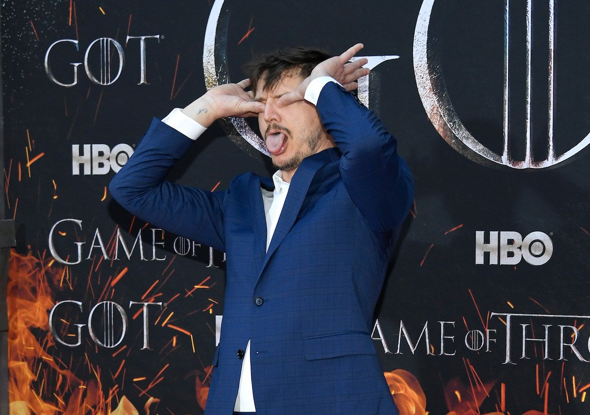 Pedro Pascal poses with his thumbs over his eyes in front of a 