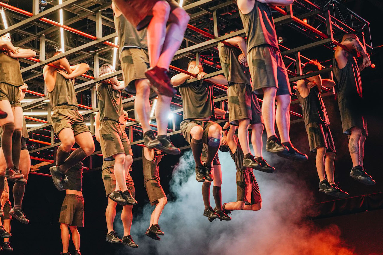 The 'Physical 100' cast hold themselves up in red metal bars.