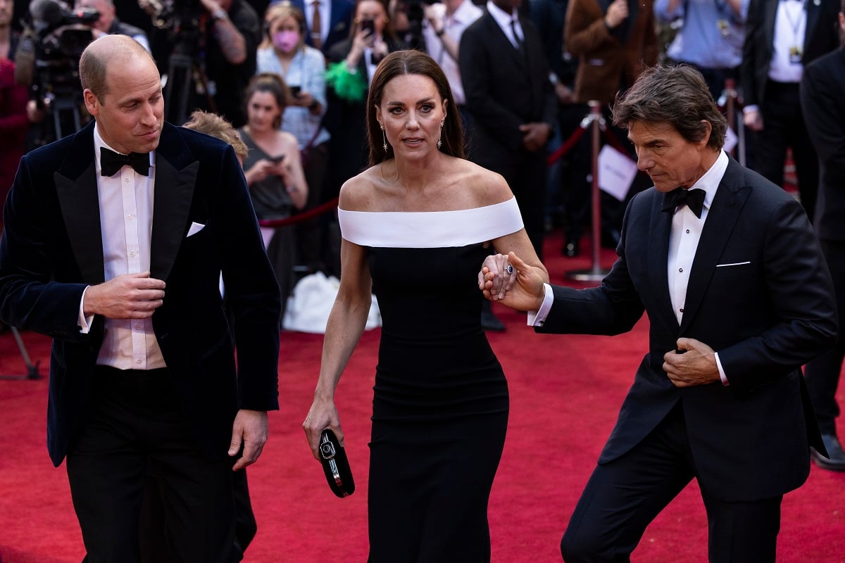 Prince William looking on as Tom Cruise grabs Kate Middleton's hand to walk up the stairs after they arrive at the Top Gun Maverick premiere