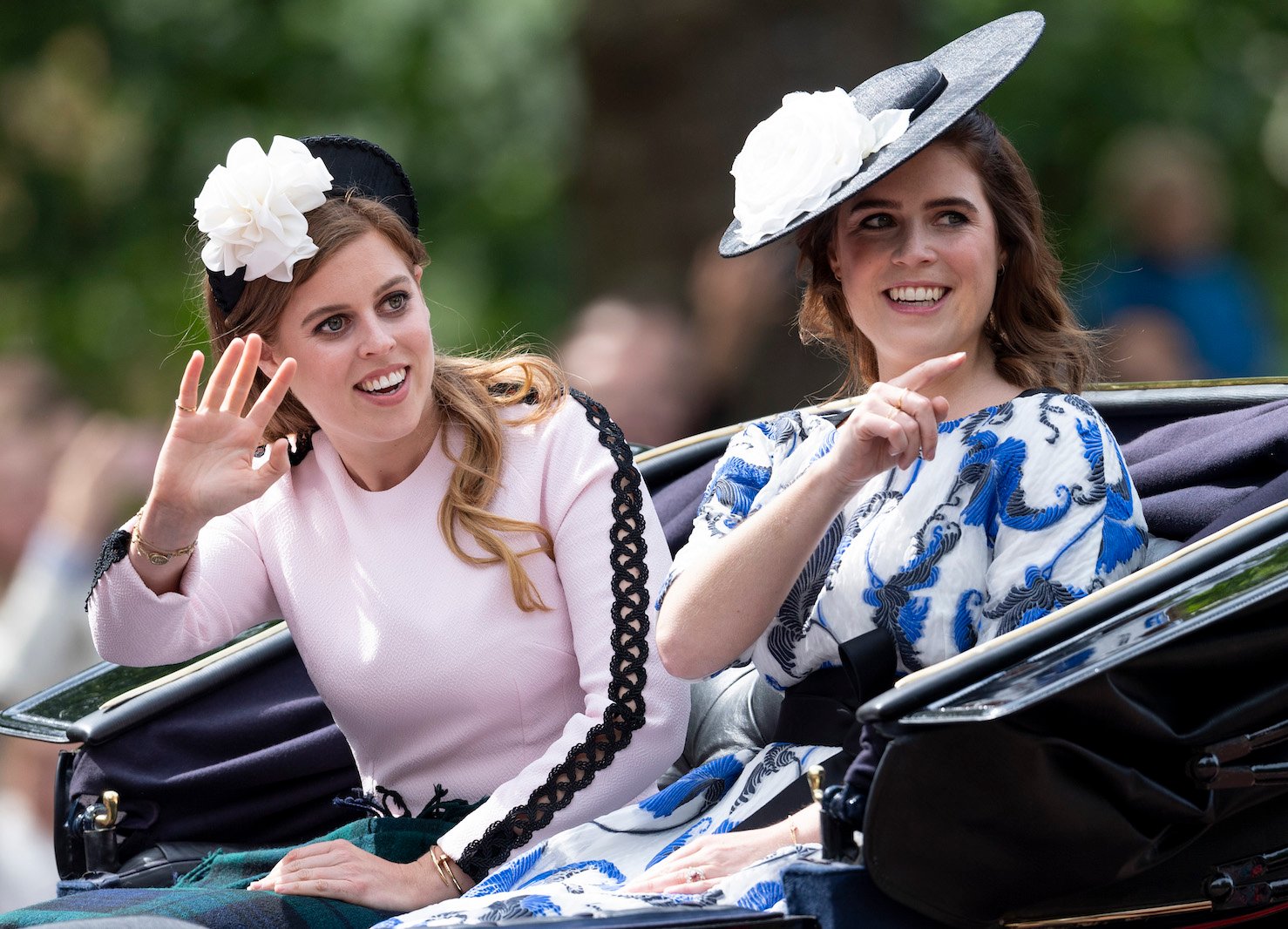 Princess Eugenie and Princess Beatrice smiling and waving in a carriage