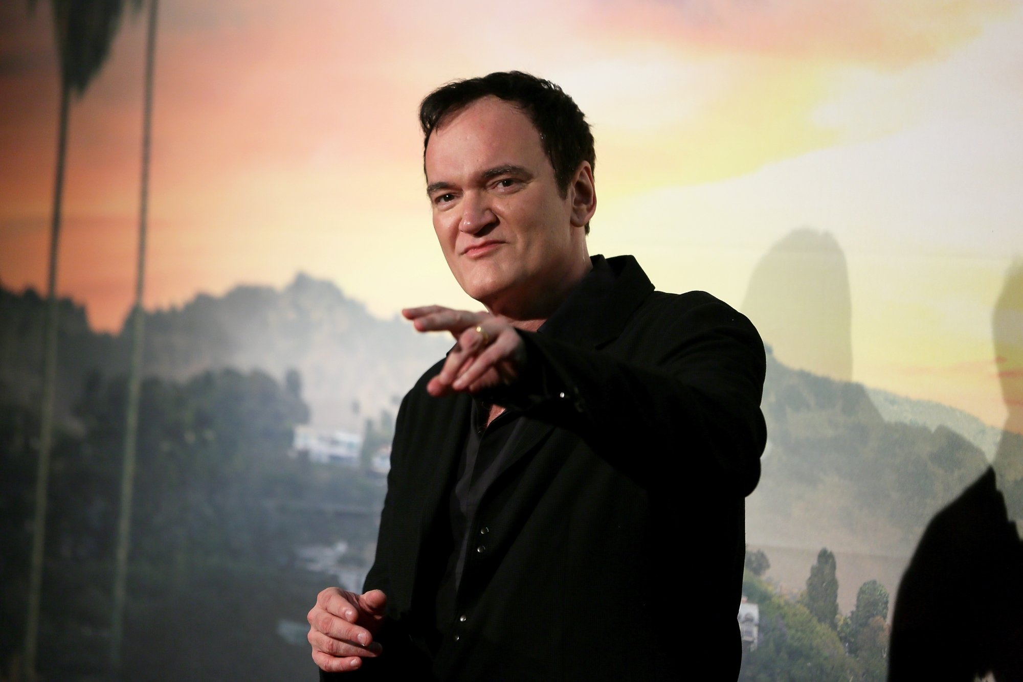 Quentin Tarantino in 'Once Upon a Time in Hollywood' premiere, which tipped its hat to 'Gunsmoke.' He's holding his hand out in front of a picture of the Hollywood Hills.