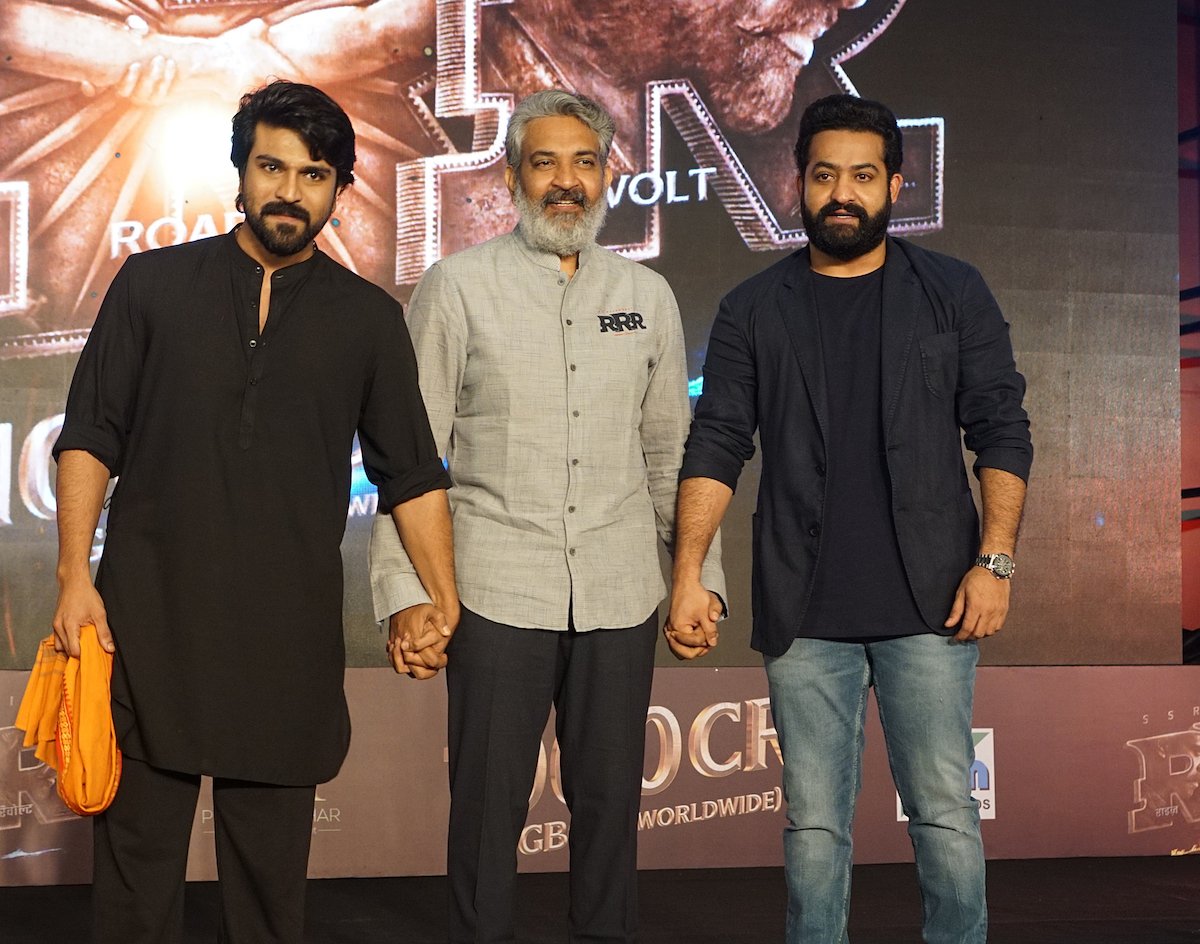 Ram Charan, S.S. Rajamouli and NTR Jr. pose in front of the "RRR" logo an 'RRR' event