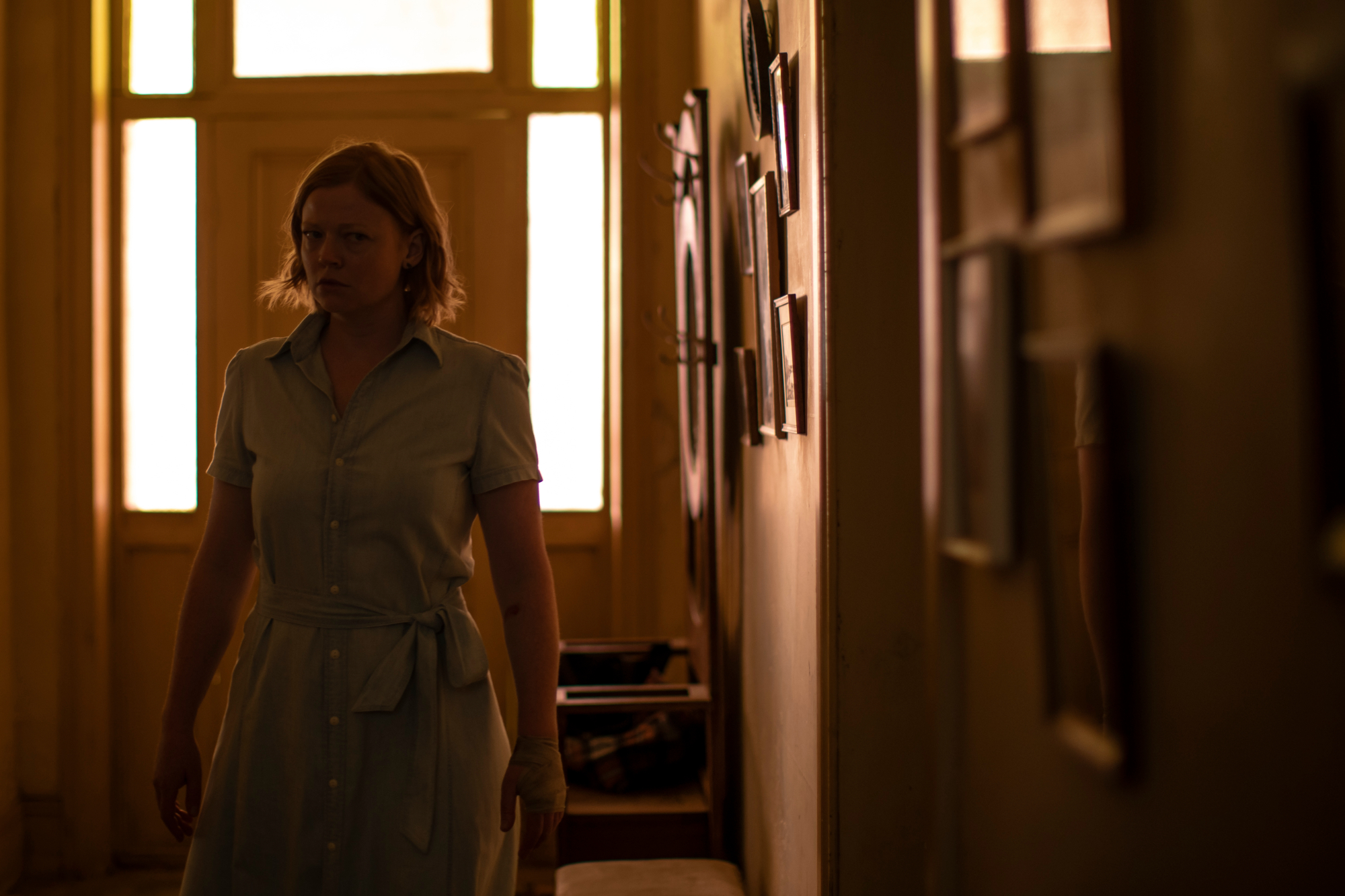 'Run Rabbit Run' Sarah Snook as Sarah looking worried, standing in a dark hallway with pictures on the wall