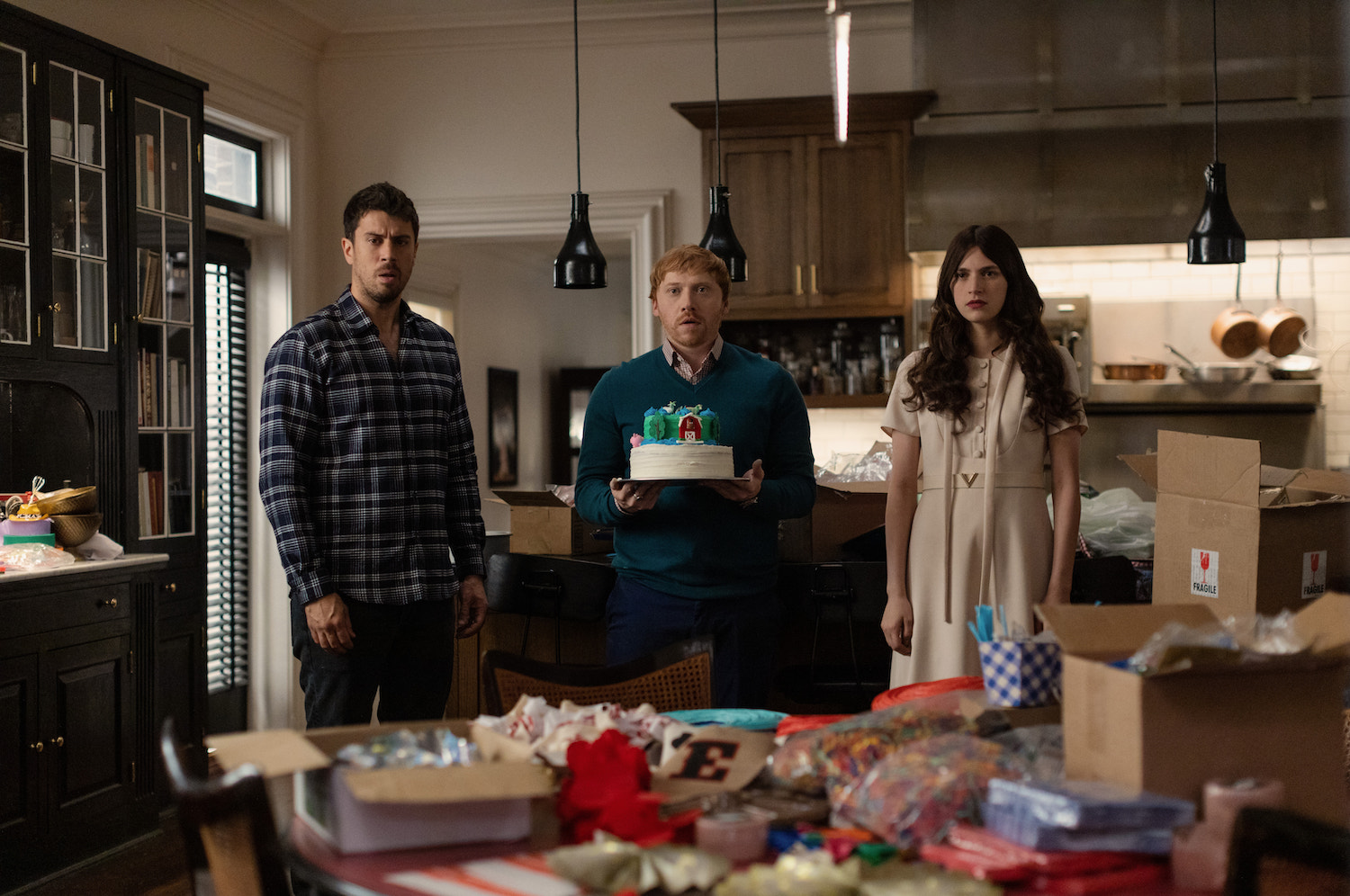 'Servant' Season 4 production still featuring Toby Kebbell, Rupert Grint, and Nell Tiger Free standing in the Turner's kitchen while Julian holds a cake.