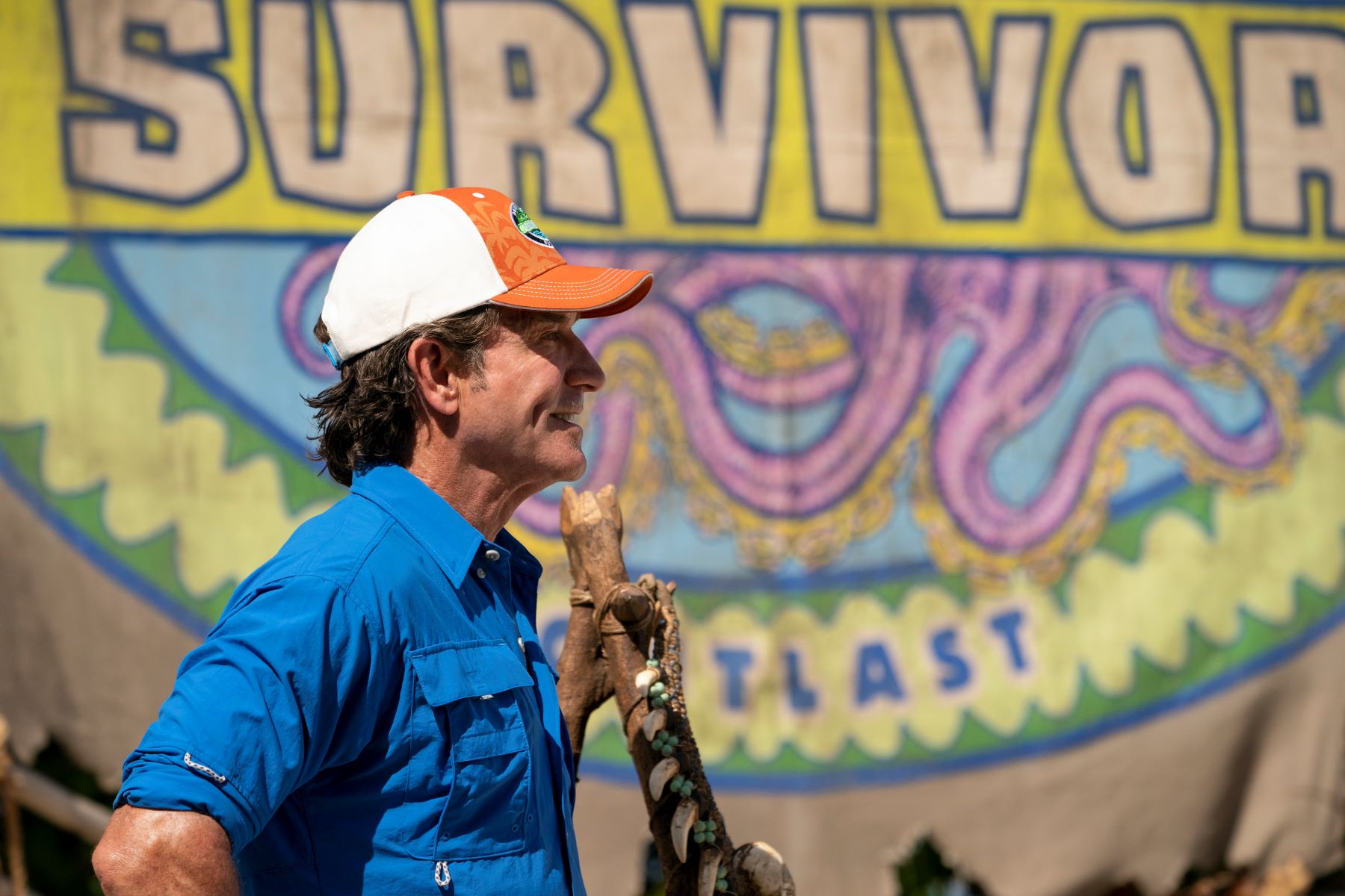Jeff Probst, the host of 'Survivor' on CBS, wears a blue button-up shirt and orange and white 'Survivor' baseball hat.
