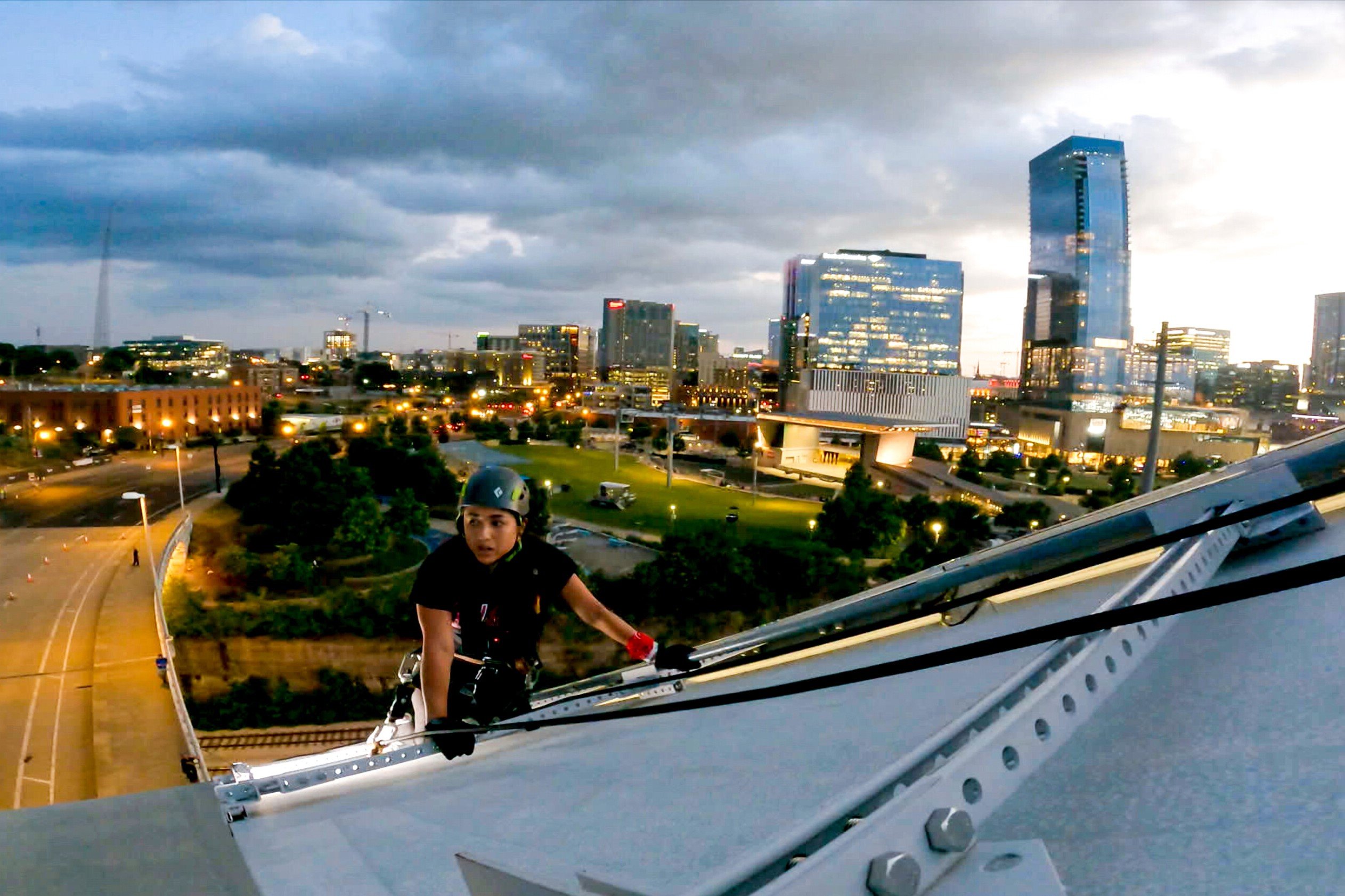 Michelle Burgos performs one of the tasks during the finale of 'The Amazing Race 34' on CBS. She scales a tall white bridge wearing a black shirt, black pants, and a dark green helmet.