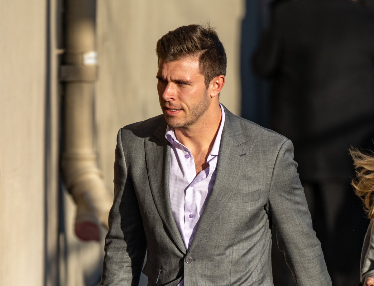 The 2023 Bachelor Zach Shallcross walks wearing a gray suit jacket and lilac button-down shirt.