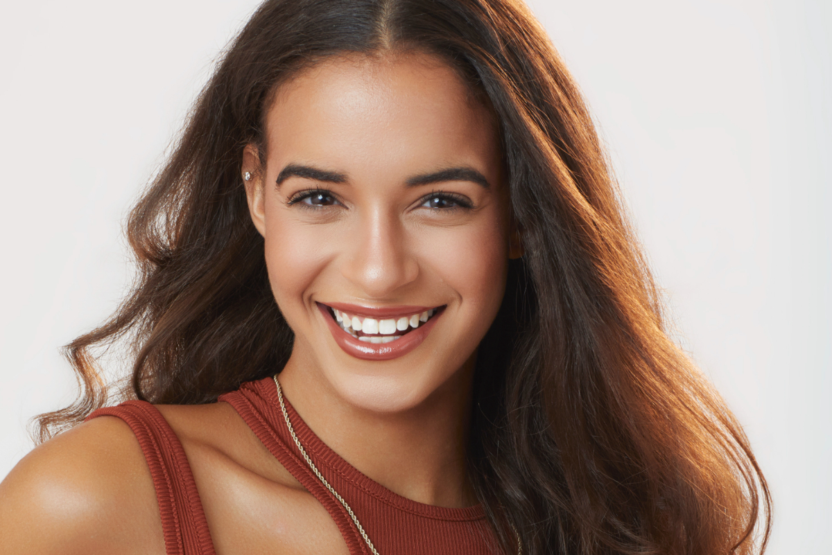 Olivia Lewis, a contestant on The Bachelor 2023, wears a burnt orange top. She has brown hair and eyes. 