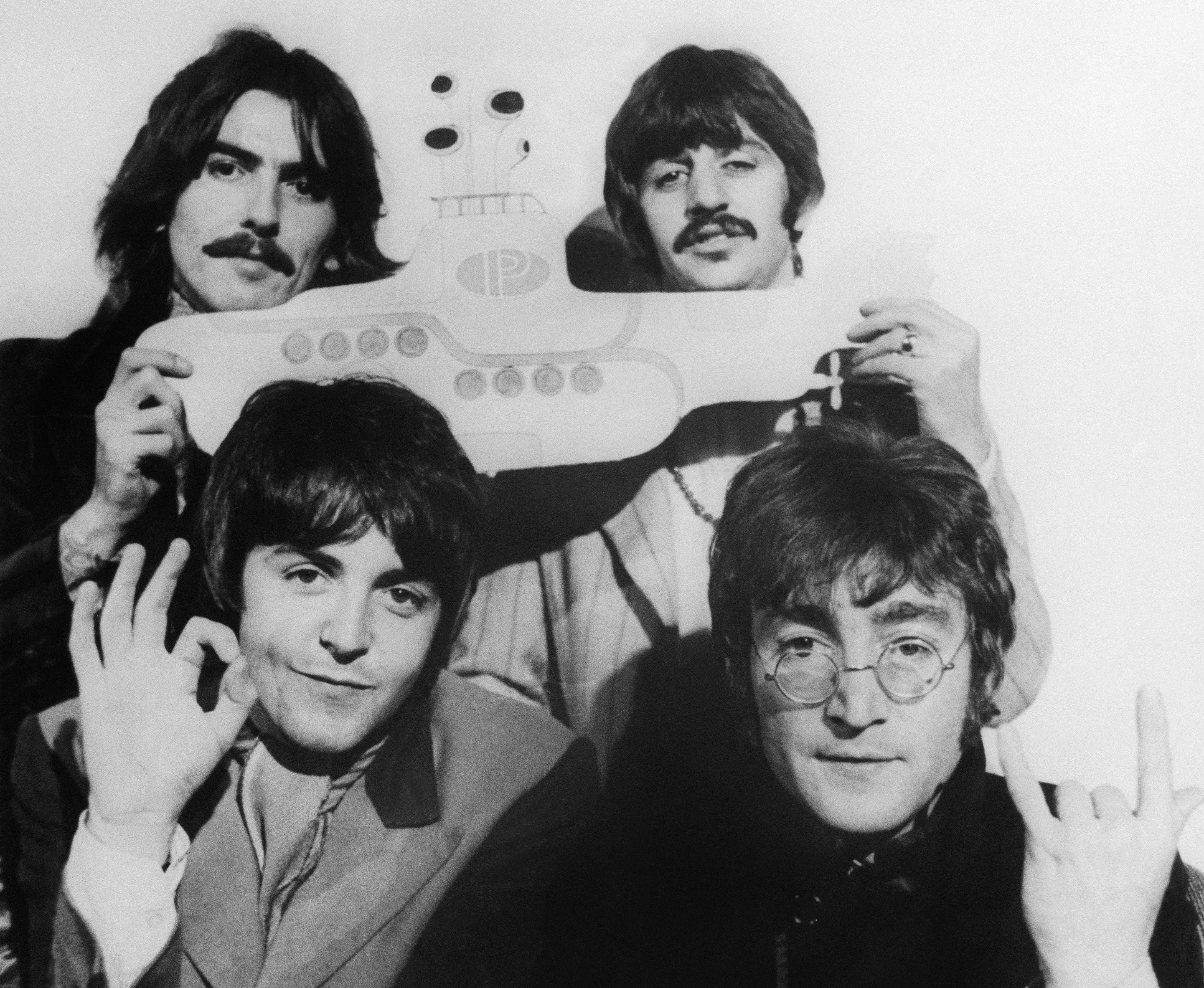 A black and white picture of The Beatles posing together. George Harrison and Ringo Starr hold a yellow submarine.