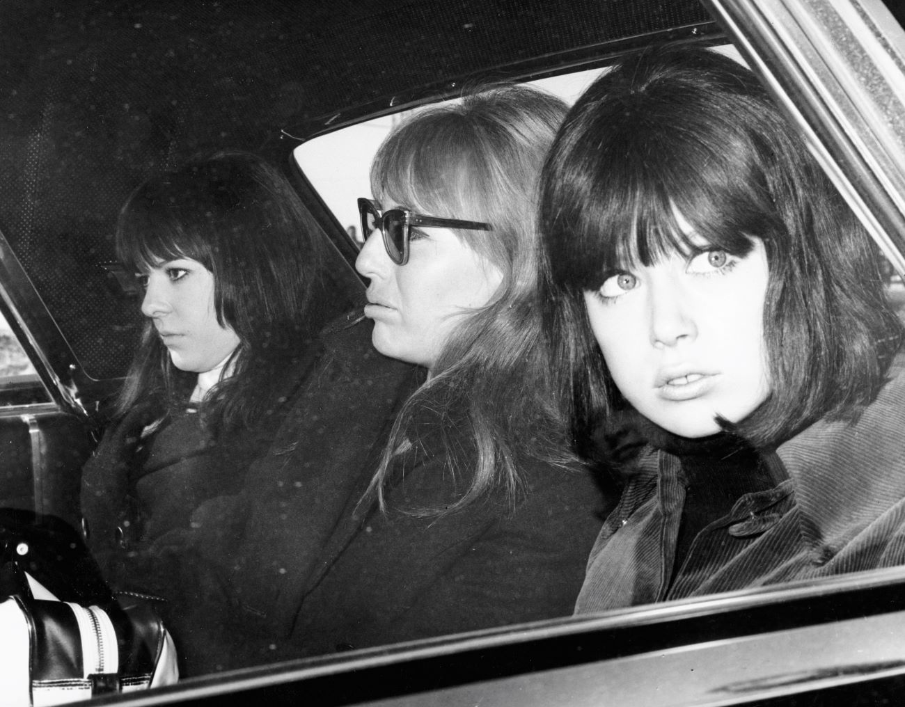 A black and white picture of Maureen Starkey, Cynthia Lennon, and Pattie Boyd sitting in a car together.
