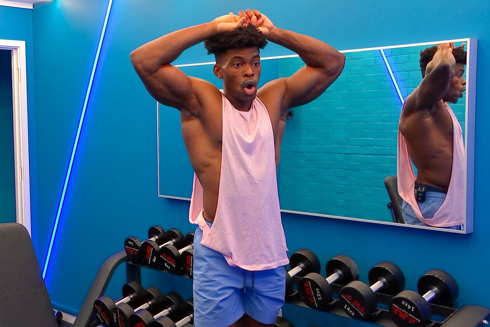 Marvin Achi, who is a part of the cast of 'The Circle' Season 5 on Netflix, wears a light pink tank top and blue shorts.