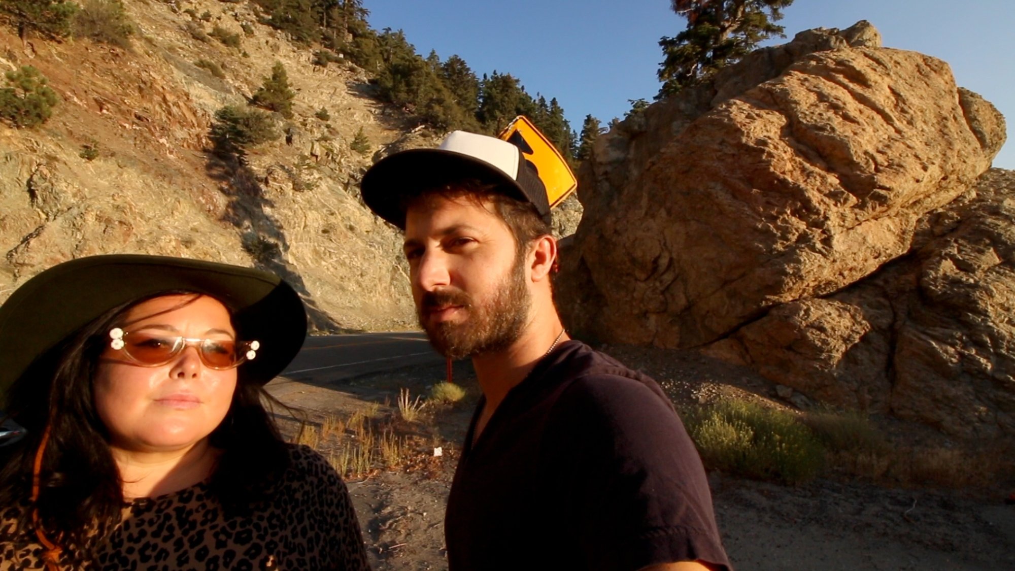 'The Outwaters' Angela Basolis as Ange Bocuzzi and Robbie Banfitch as Robbie Zagorac looking at the camera standing in front of a dirt road and a rocky mountainside