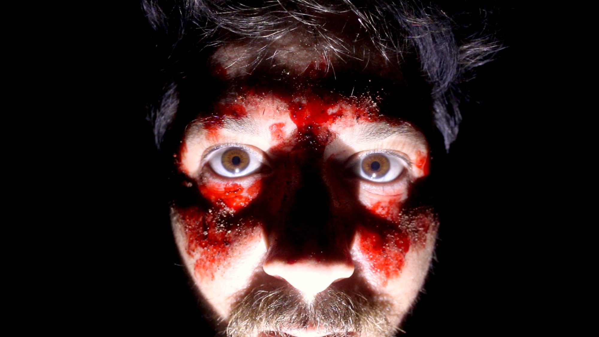 'The Outwaters' Robbie Banfitch as Robbie Zagorac looking into the camera surrounded by darkness with blood on his face