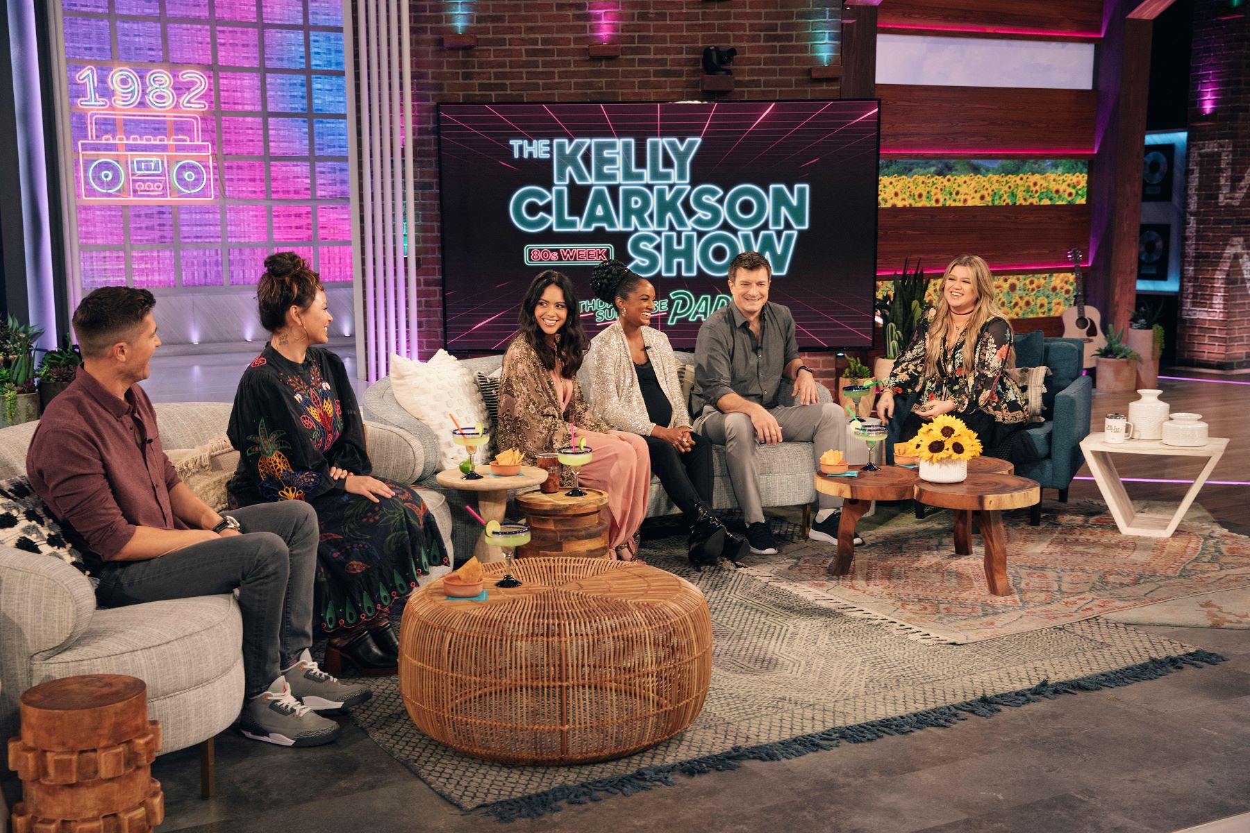 Eric Winter, Melissa O'Neil, Alyssa Diaz, Mekia Cox, Nathan Fillion, and Kelly Clarkson, who will all star in 'The Rookie' Season 5 Episode 12, appear on 'The Kelly Clarkson Show.' Winter and O'Neil sit on the couch on the left, Diaz, Cox, and Fillion sit on the couch in the middle, and Clarkson sits in an armchair on the right.