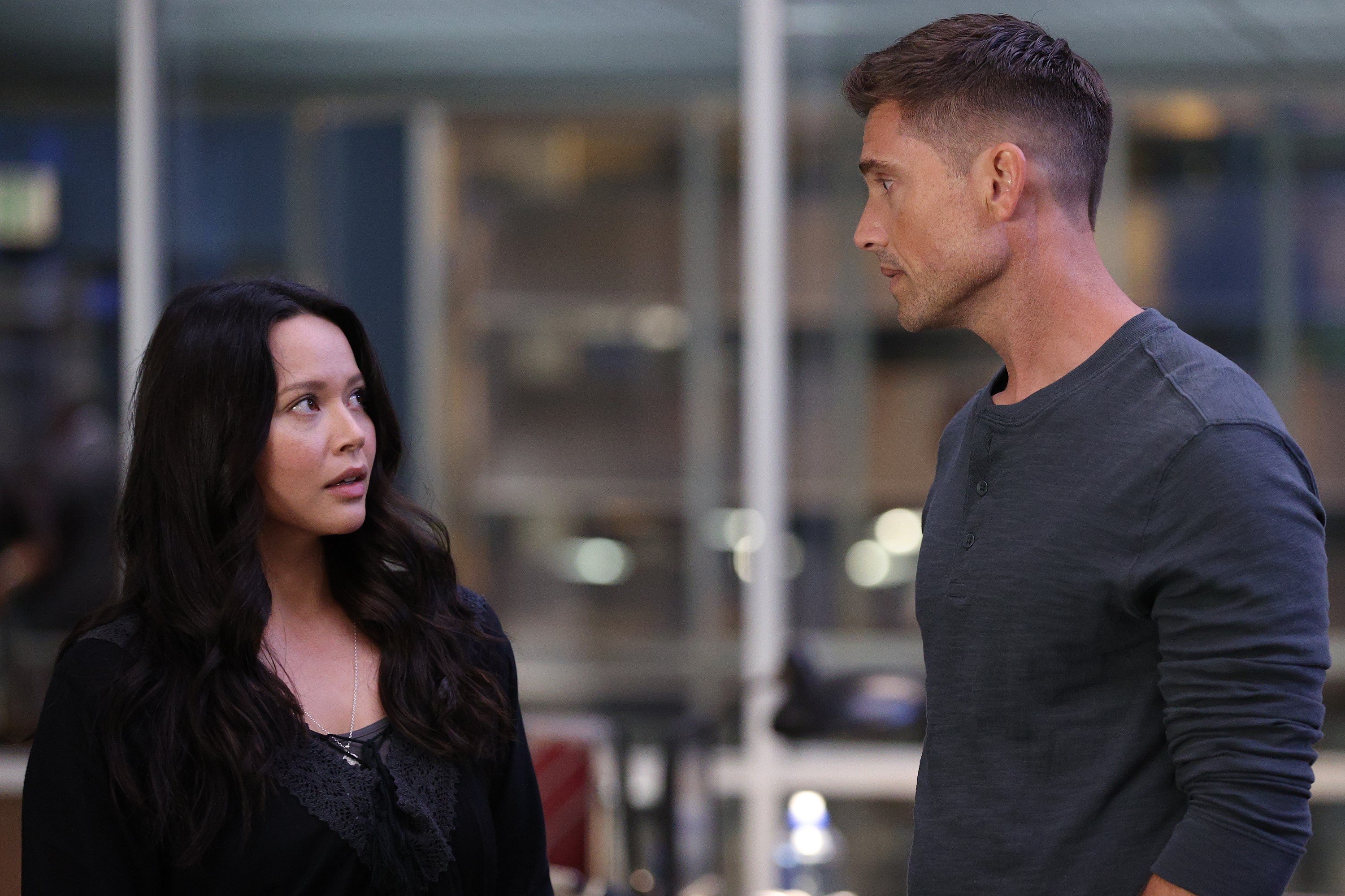 Melissa O'Neil and Eric Winter star as Lucy Chen and Tim Bradford in 'The Rookie' Season 5 on ABC. In the photo, they share a scene in season 4 where Lucy wears a black long-sleeved top and Tim wears a dark gray henley shirt.