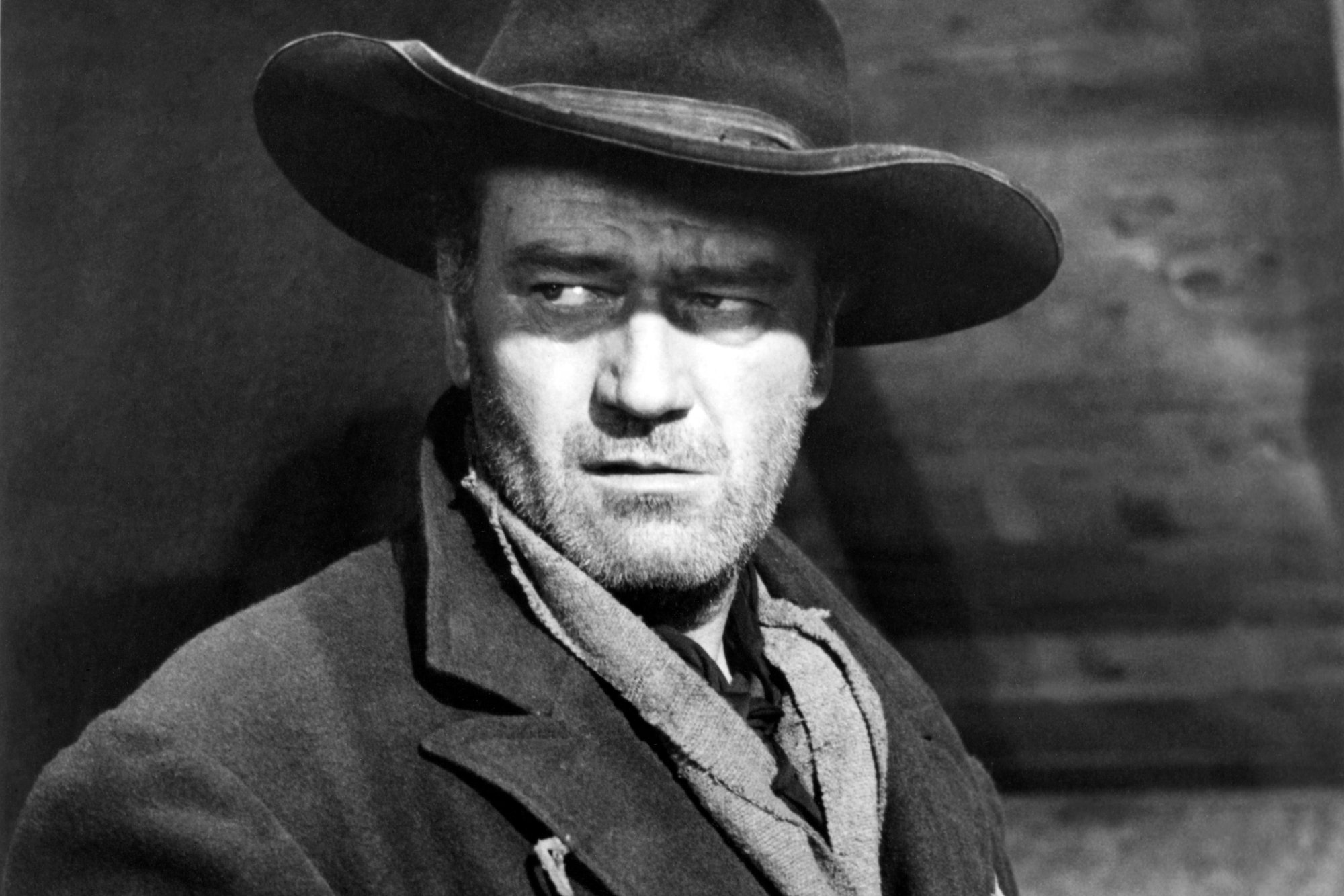 'The Searchers' John Wayne as Ethan Edwards in a black-and-white picture looking off to the side while wearing a cowboy costume