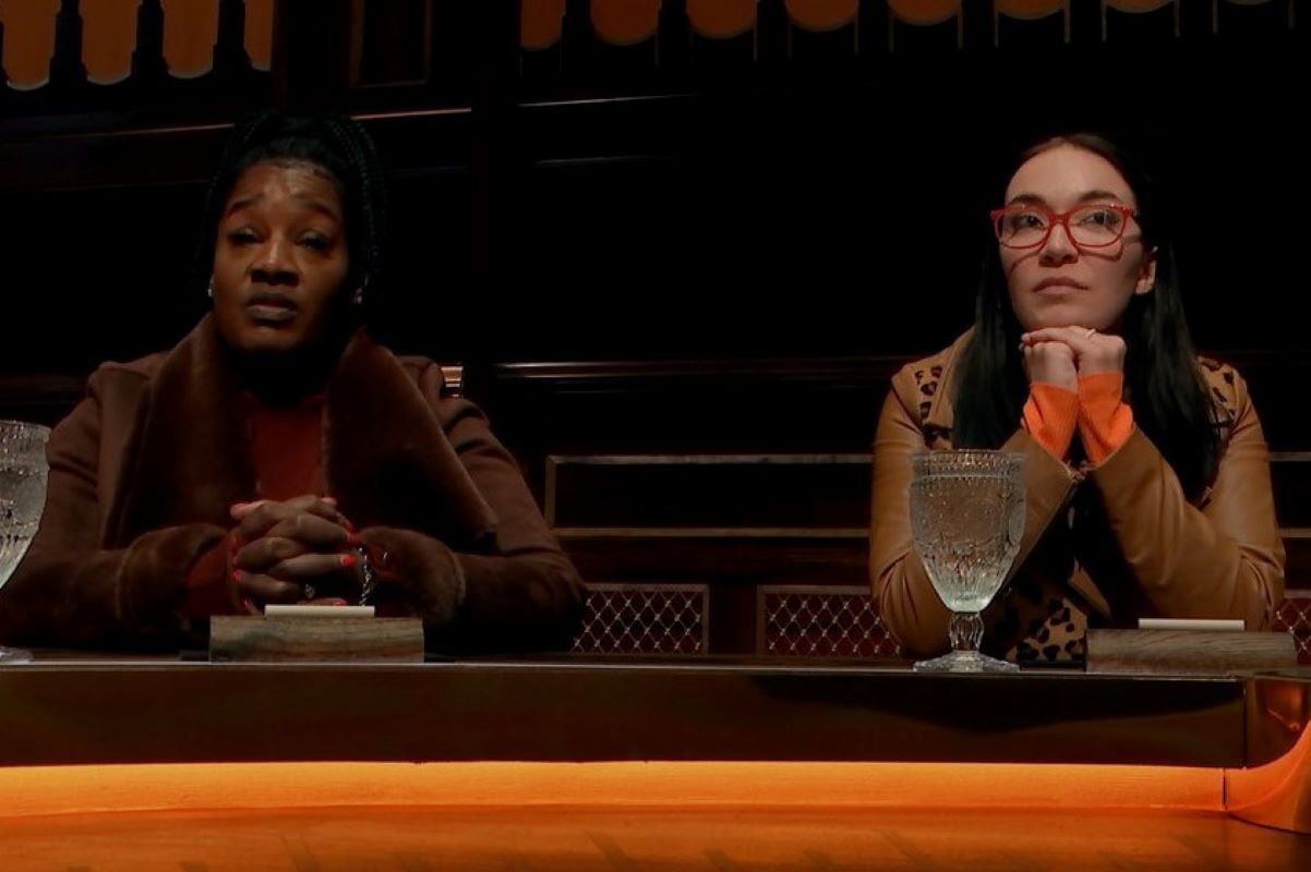 Cirie Fields and Amanda Clark, who starred in 'The Traitors' on Peacock, sit next to each other at the round table. Cirie wears a brown coat over a red sweater. Amanda wears a brown leopard print jacket and red-framed glasses.