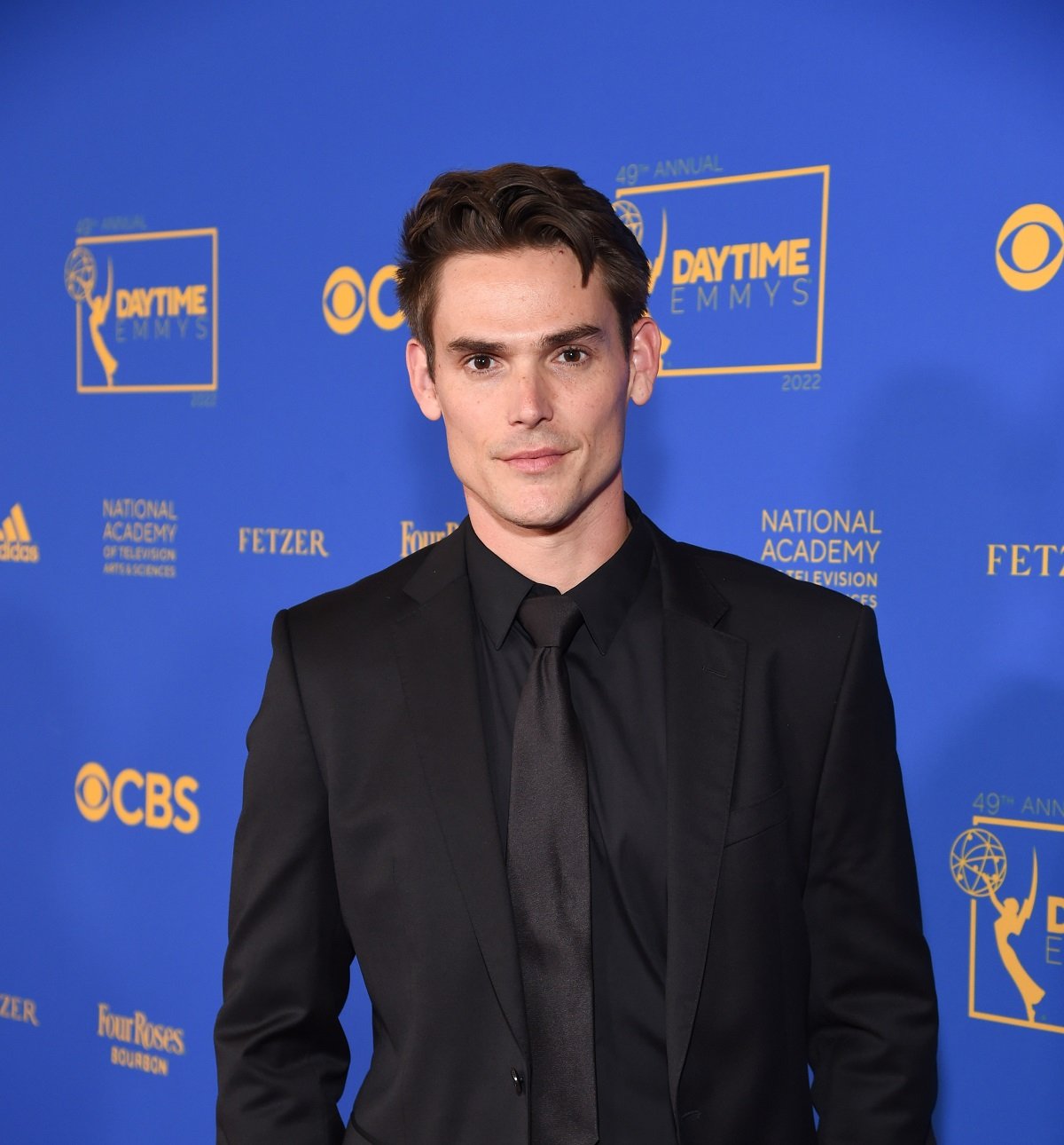 'The Young and the Restless' star Mark Grossman dressed in a black suit; posing on the red carpet of the 2022 Daytime Emmys.