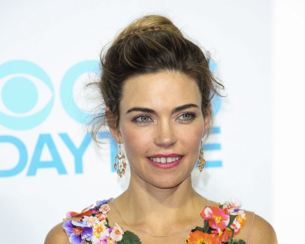 'The Young and the Restless' star Amelia Heinle wearing an orange floral dress; smiles for a photo.