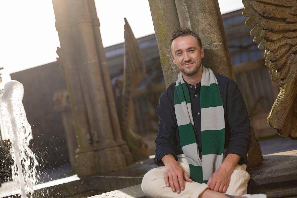 Wearing a Slytherin striped scarf, Tom Felton unveils the new Professor Sprout's Greenhouse feature at Warner Bros. Studio Tour in 2022