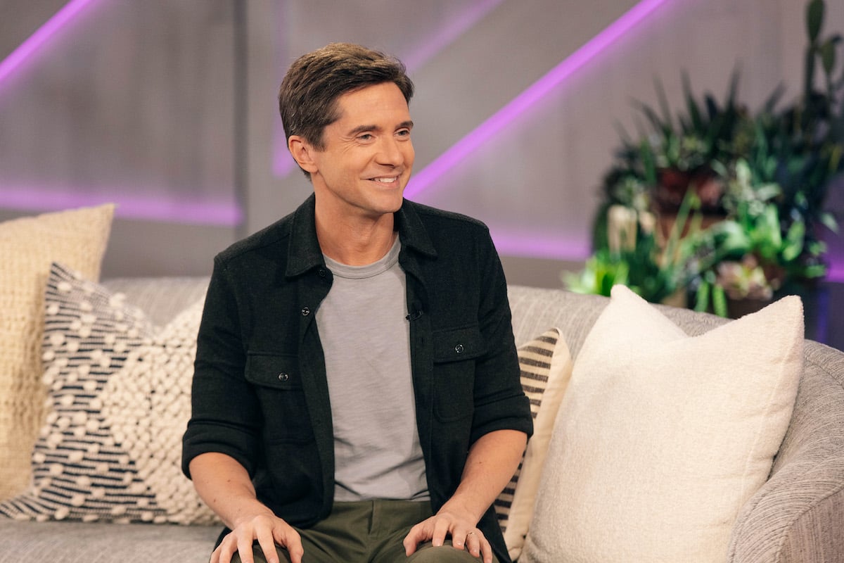 Topher Grace smiling, sitting on a couch
