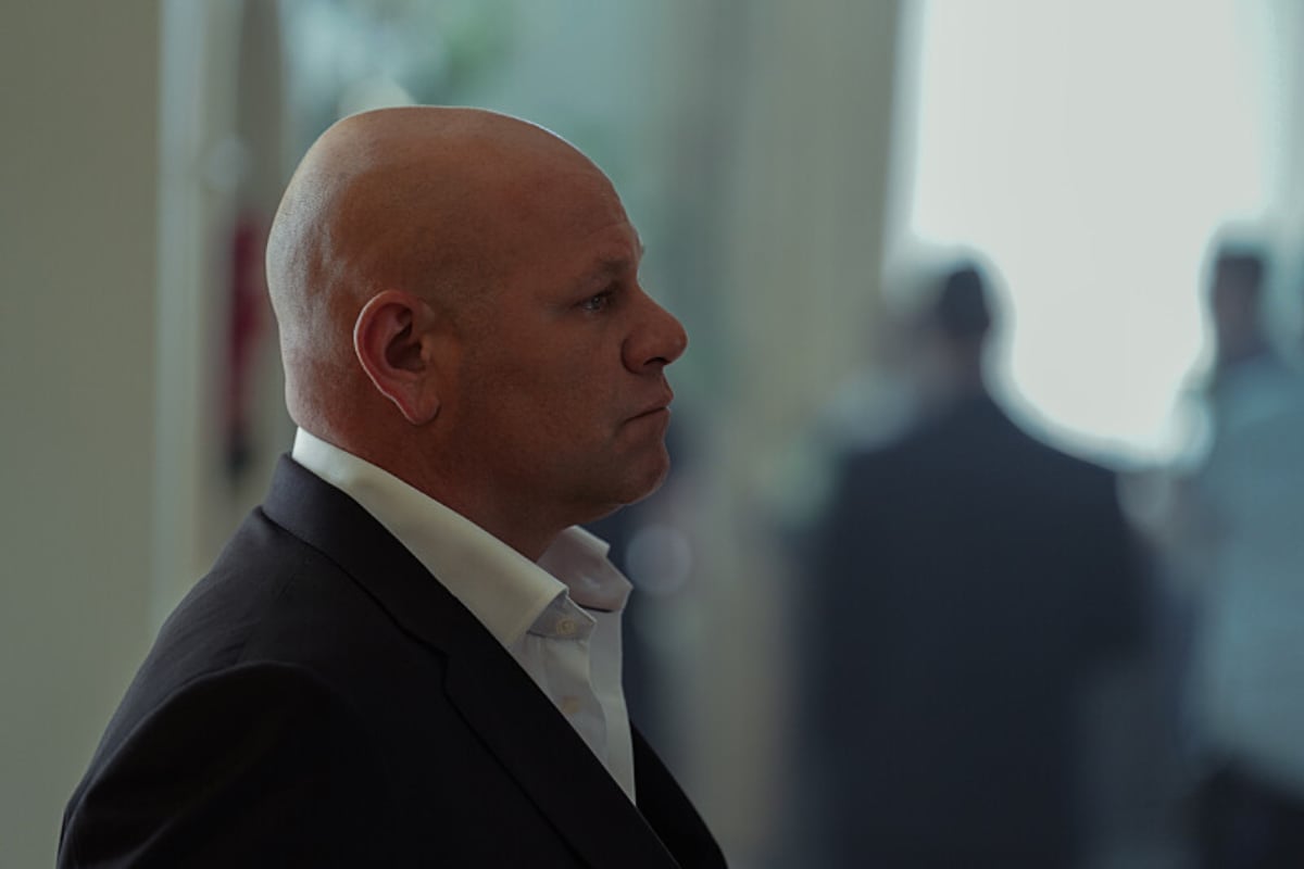 Domenick Lombardozzi as Chickie Invernizzi in Tulsa King. Chickie wears a black suit jacket and white collared shirt and has a shaved head. 